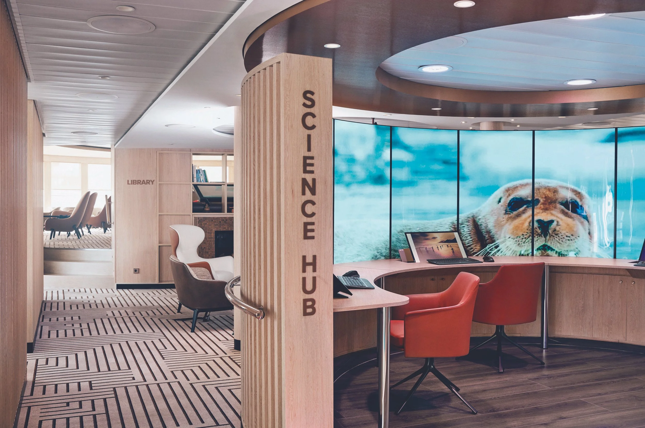 A modern library reception area named Science Hub with multiple workstations and a large digital screen displaying a seal's face.