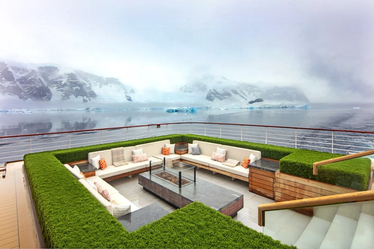 Outdoor seating area on a boat with views of icy mountains and icebergs over water.
