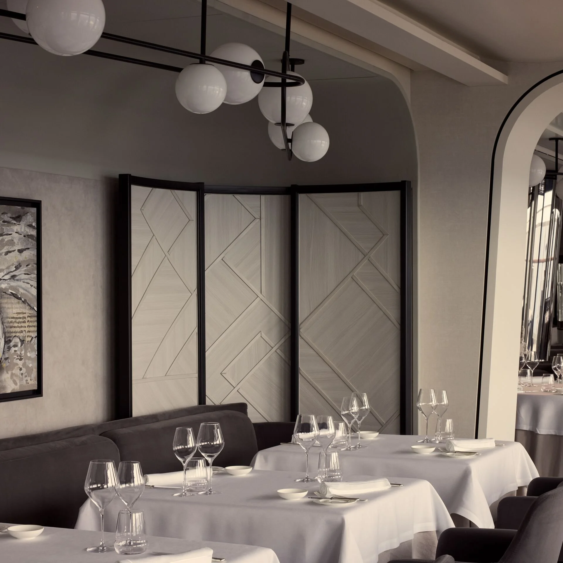 Elegant restaurant interior with white tablecloths, wine glasses, and modern lighting fixtures.