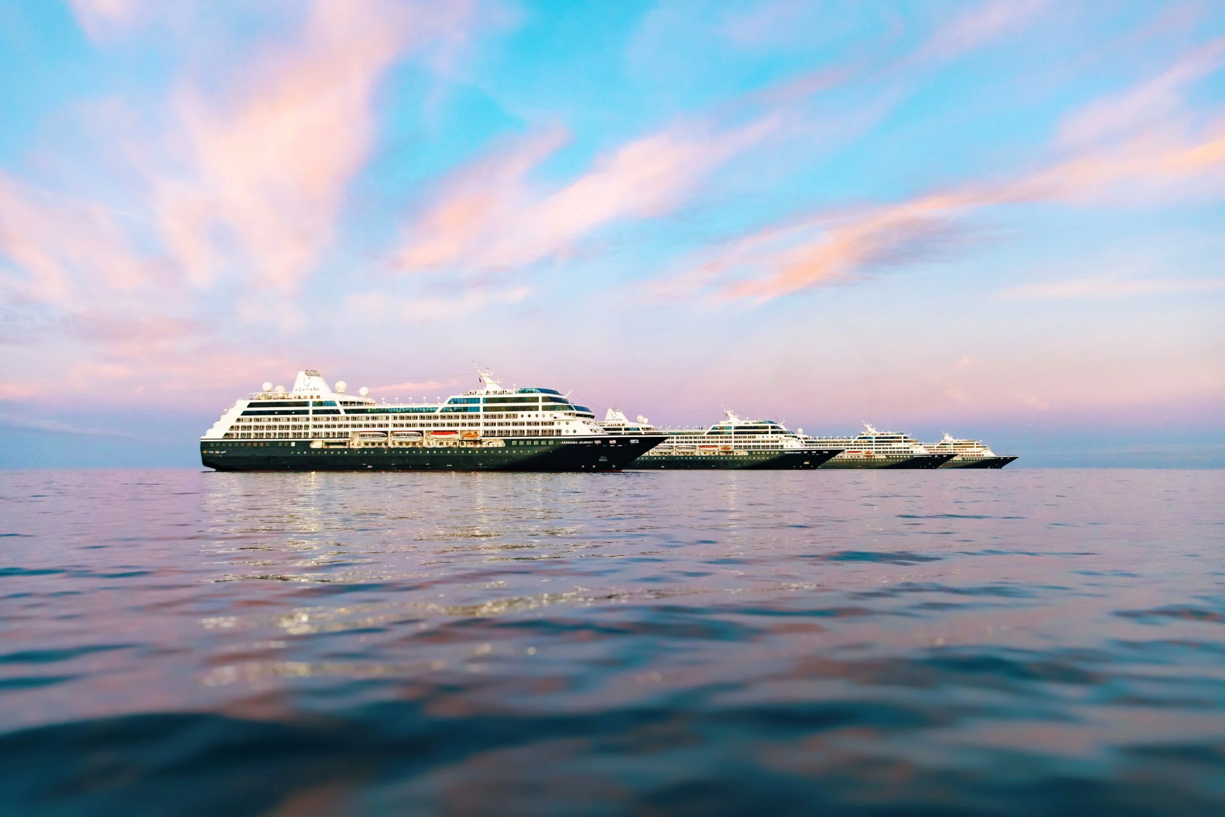 Two large cruise ships floating on calm ocean waters under a partly cloudy sky during sunset.