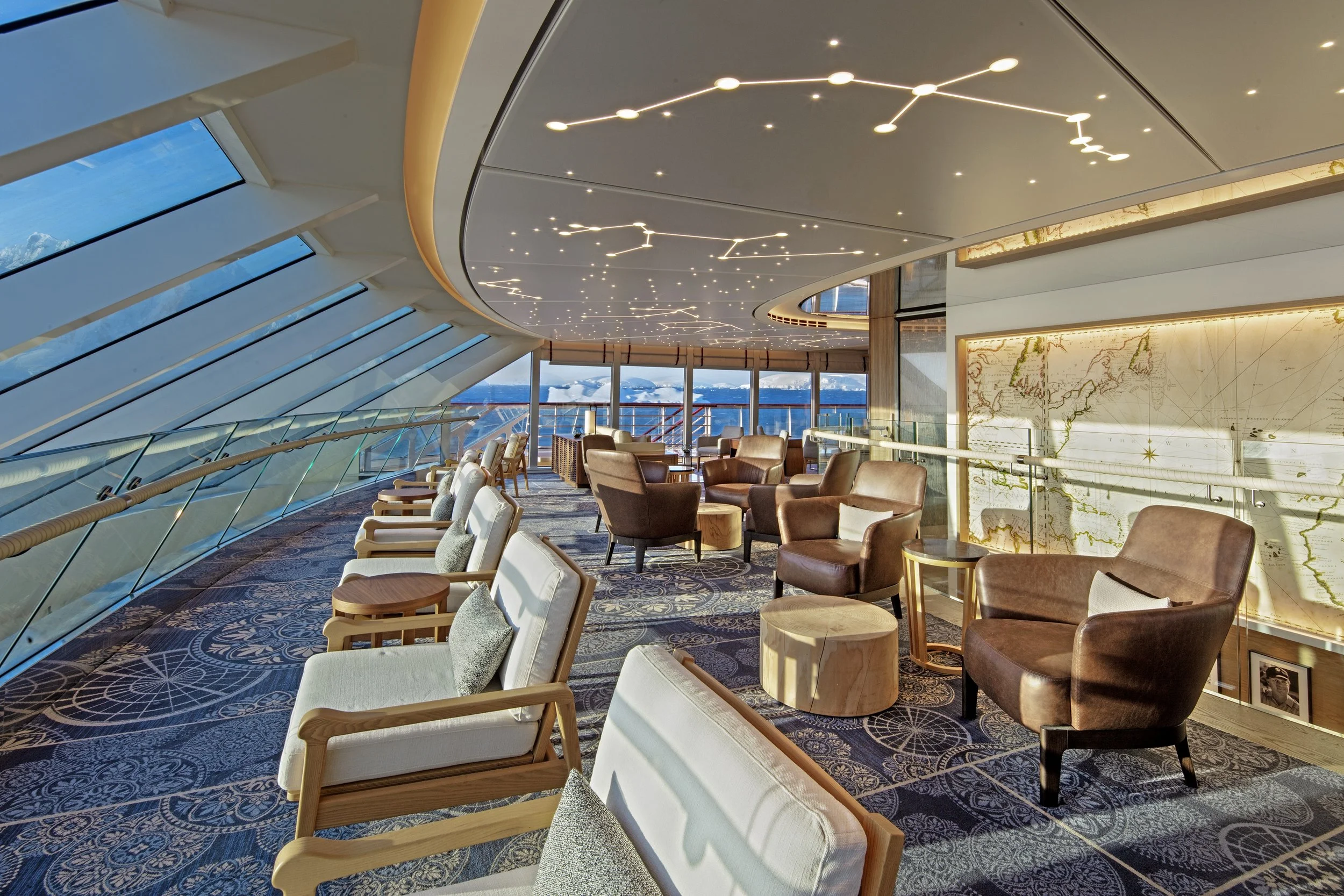 Luxurious lounge area with comfortable chairs and tables, large windows with a view of snowy mountains, modern ceiling lights, and wall decor featuring a world map.