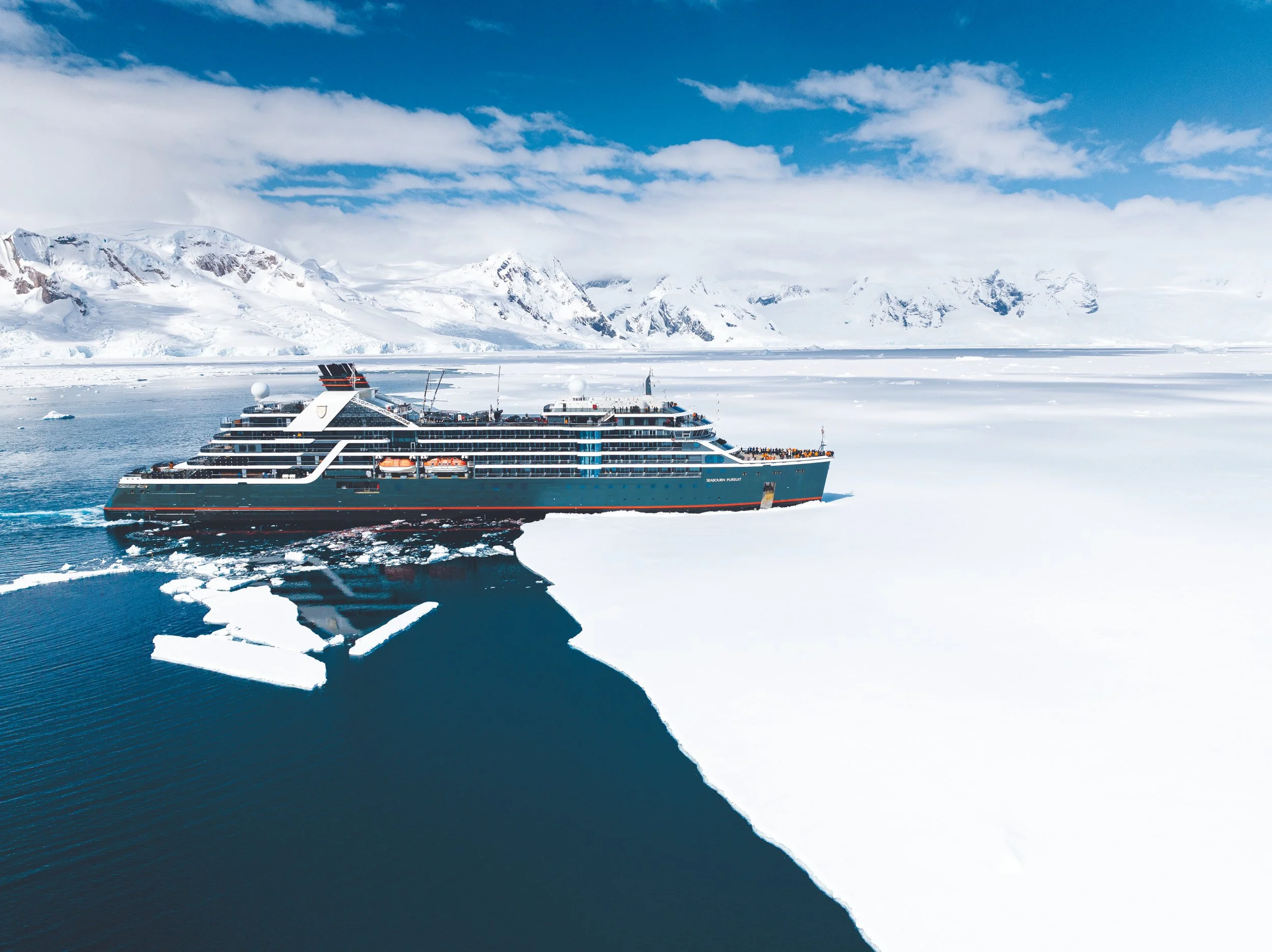 A cruise ship sailing through icy waters surrounded by snow-covered mountains and icebergs in Antarctica.