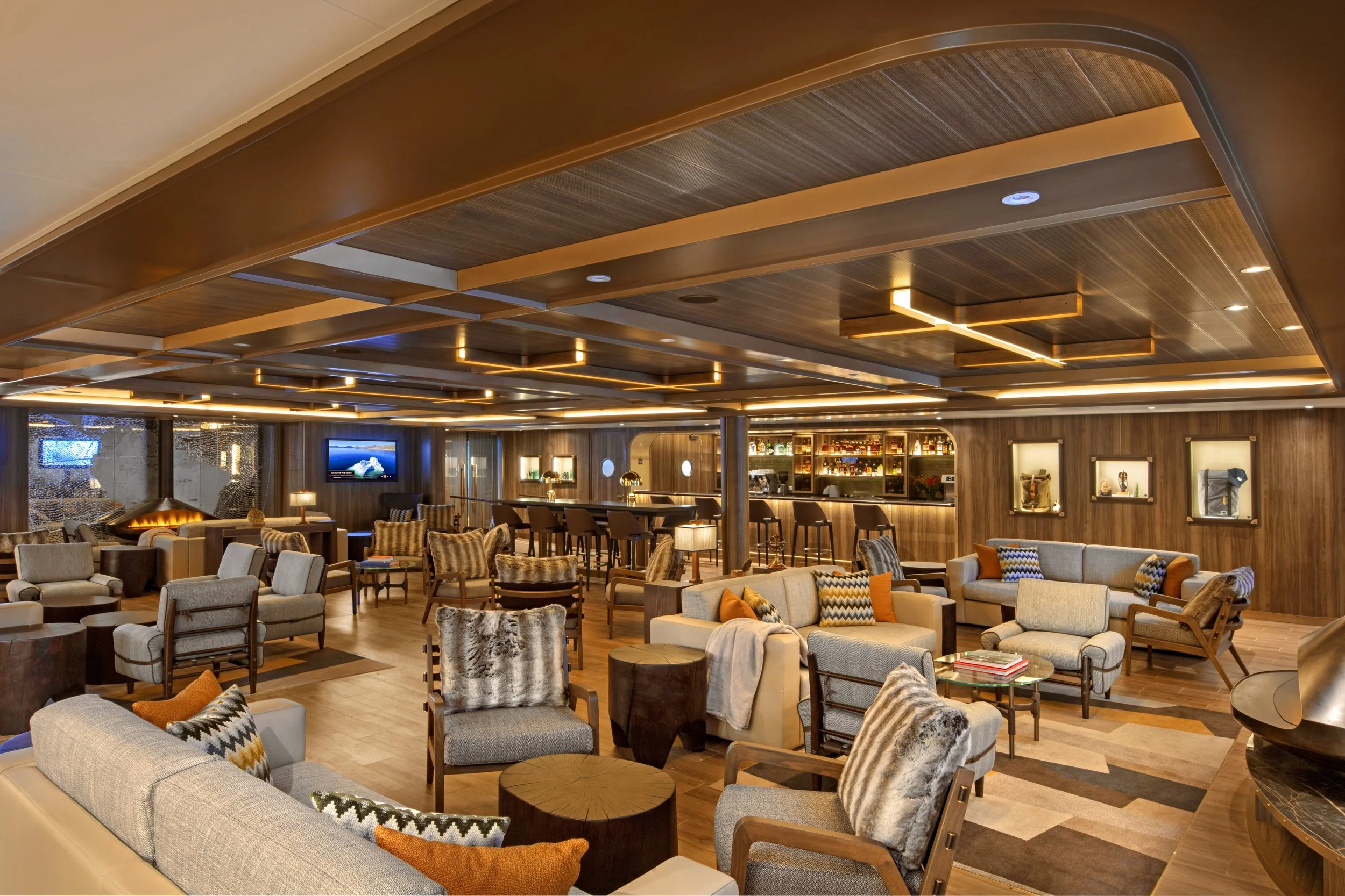Elegant hotel lounge with wooden furniture, plush chairs, sofas, and a bar area, illuminated by warm lighting.