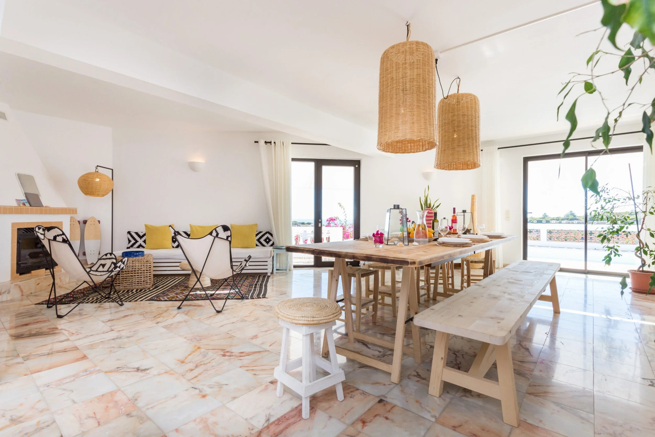 Bright living space with a dining table, chairs, and a sofa. Woven pendant lights and décor add a natural touch. Large windows with view outside.