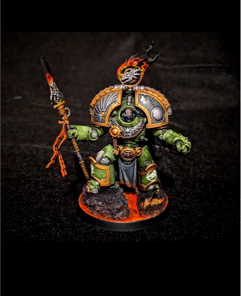 Model of a Warhammer 40k Space Marine in green armor with gold accents, holding a spear with flames, standing on a textured base.