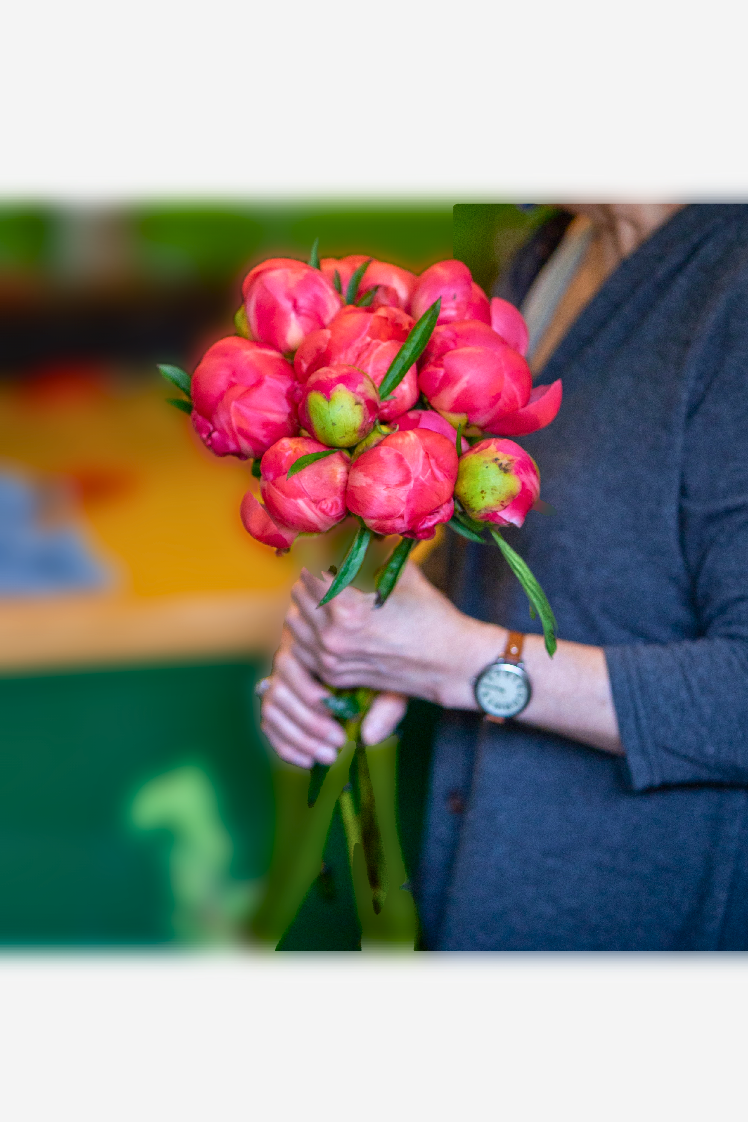 Person holding a bouquet of vibrant pink peonies with green leaves.