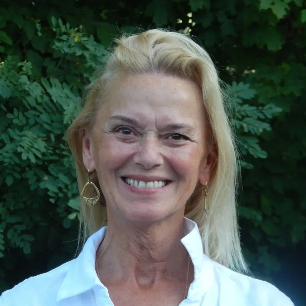 Deb Nottke with blonde hair smiling outdoors with green foliage background.
