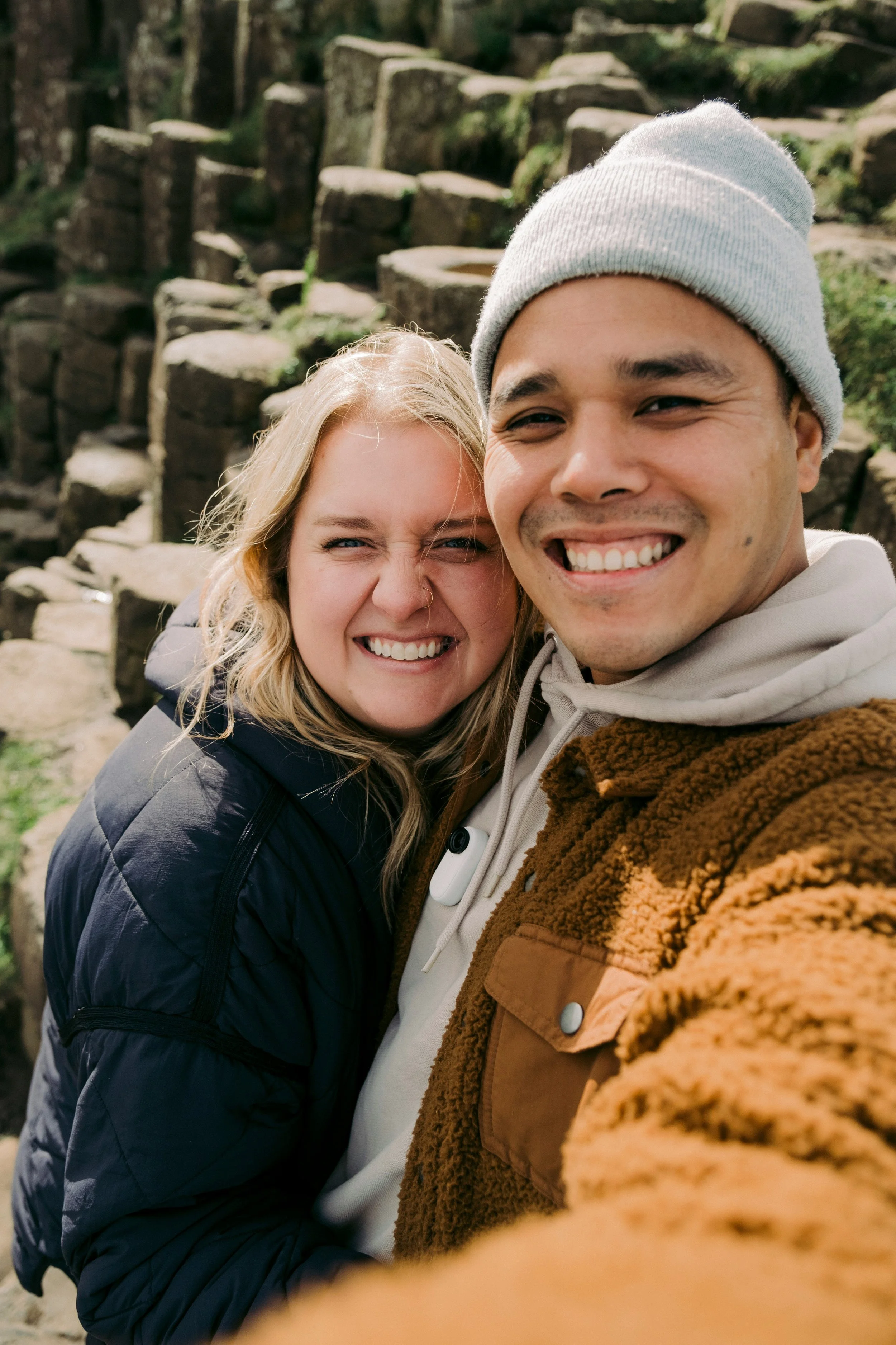 A smiling couple taking a selfie outdoors with stone steps in the background.