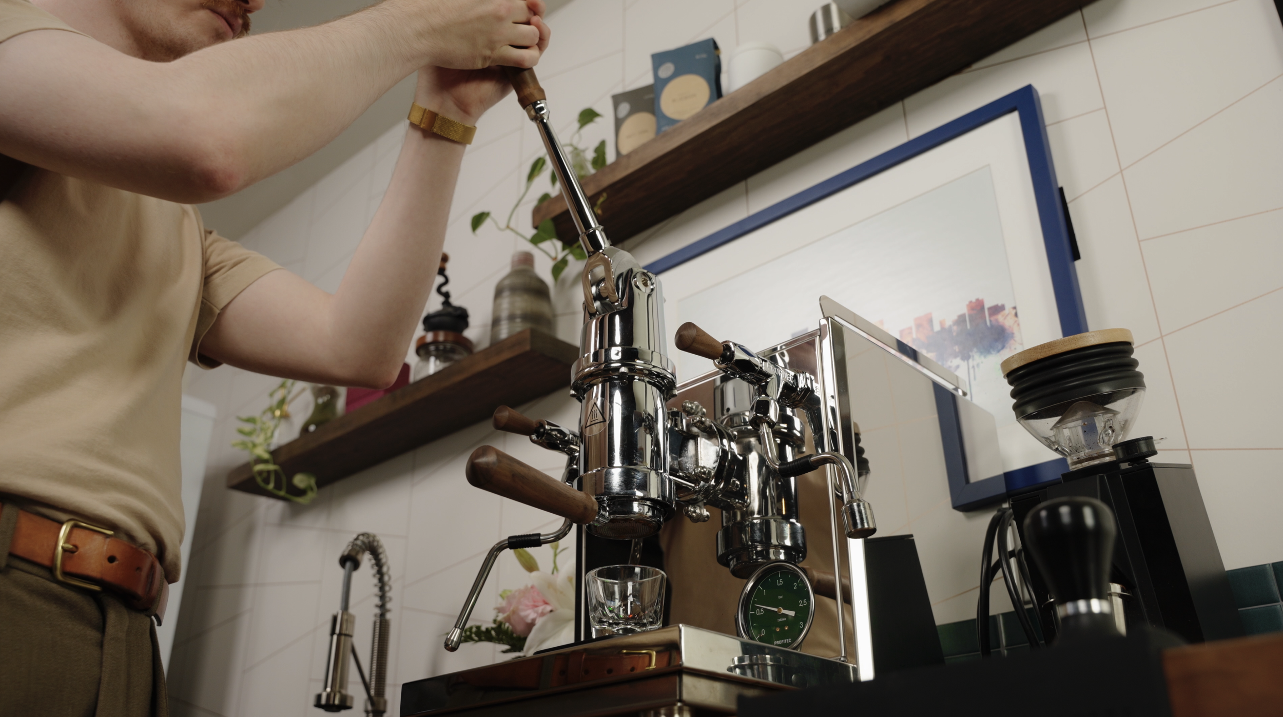 A person operating a vintage chrome espresso machine, with a glass placed under the coffee spout in a cozy kitchen setting.