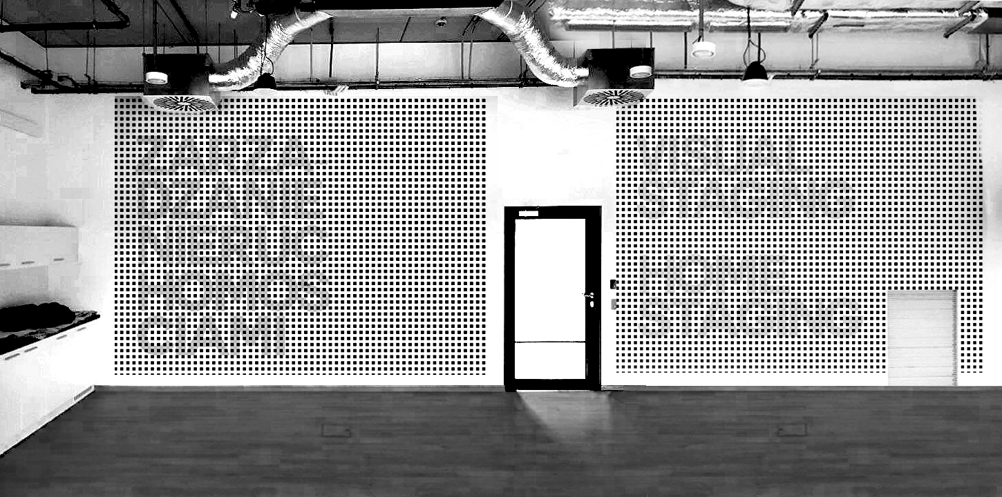 Empty room with white walls, wooden floor, black door in the center, and wall panels with small square perforations on either side. Ceiling has exposed ductwork and hanging lights.