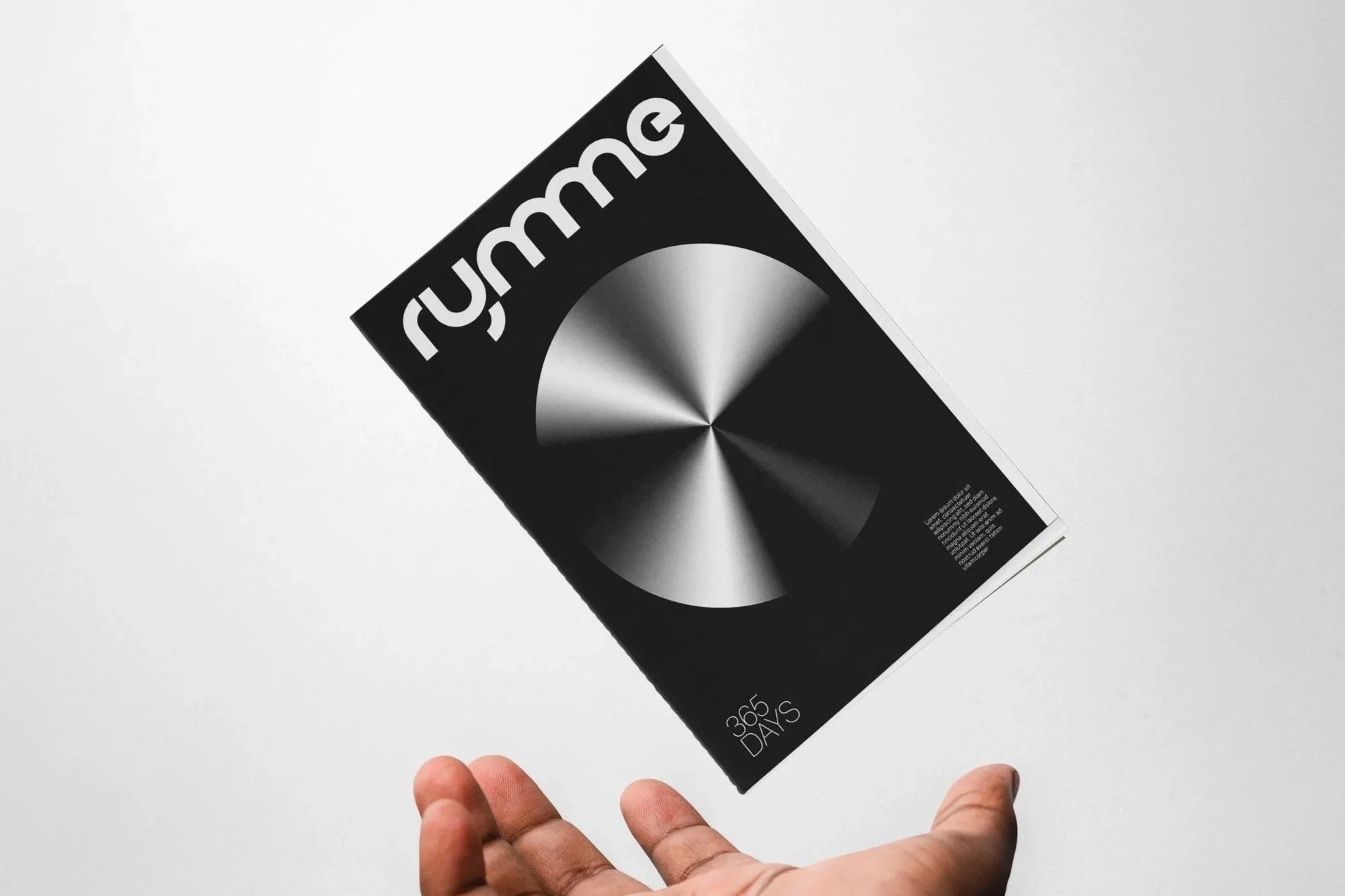 A hand holding a black booklet titled '365 DAYS' with the word 'rumme' on the cover, against a plain white background.