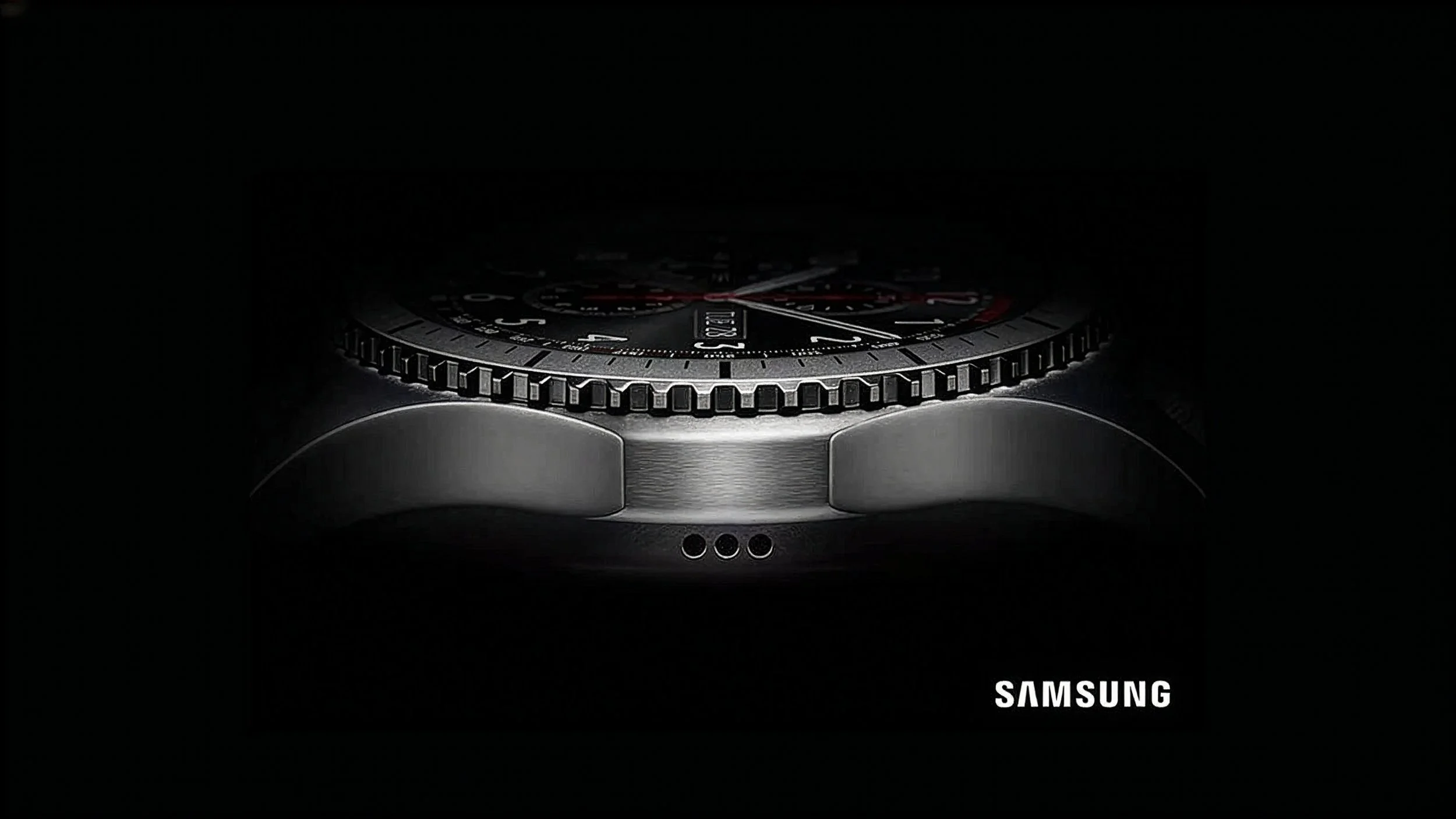 A close-up photo of a Samsung wristwatch, showing the detailed dial, bezel, and part of the stainless steel case, set against a black background.