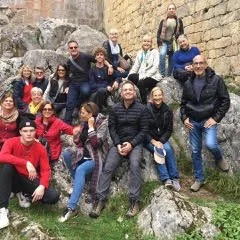 A group of people posing outdoors on rocky terrain near an ancient stone wall on a spiritual pilgrimage in France with Janet Pullen.