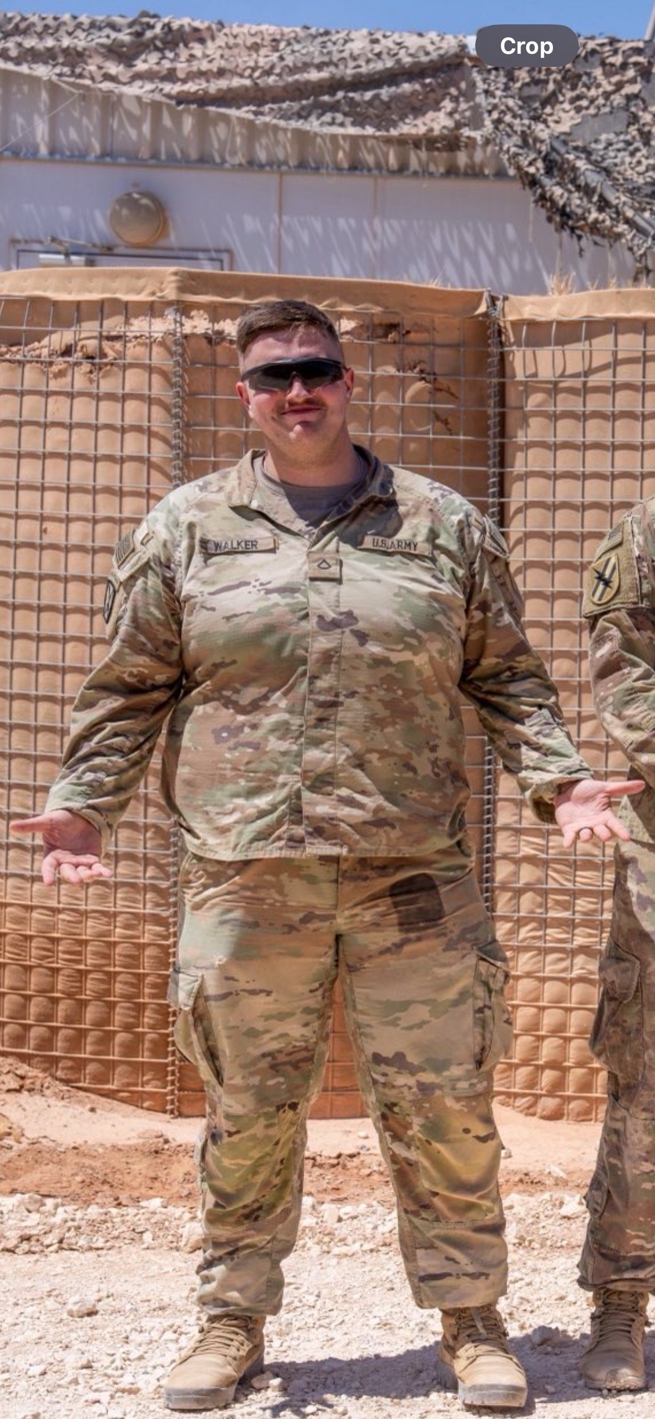 Ben Walker in a military uniform and sunglasses, standing outdoors during a deployment to the Middle East