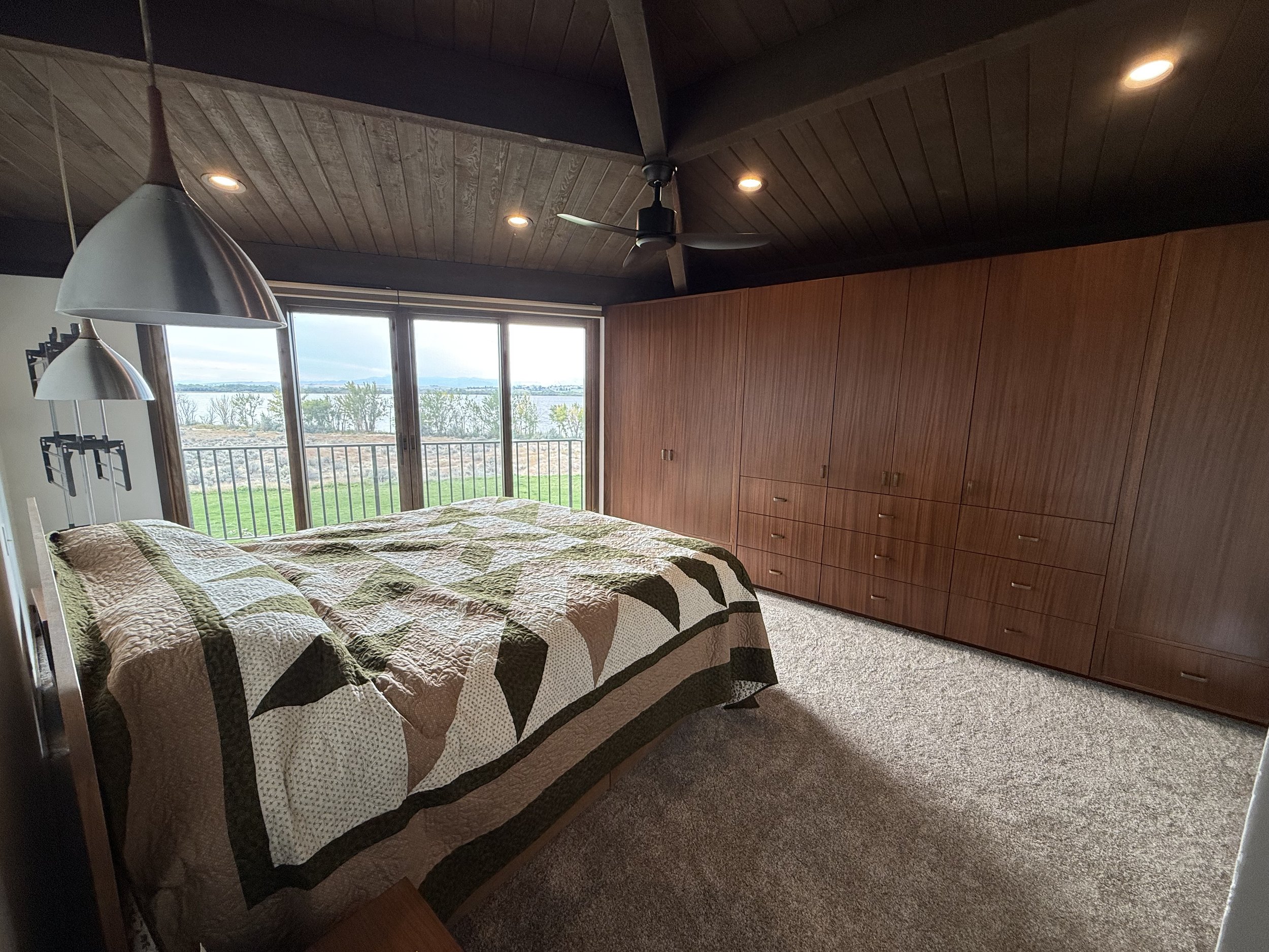 Room with built-in wooden bookshelves, open double doors leading to another room with carpeted floor and windows.