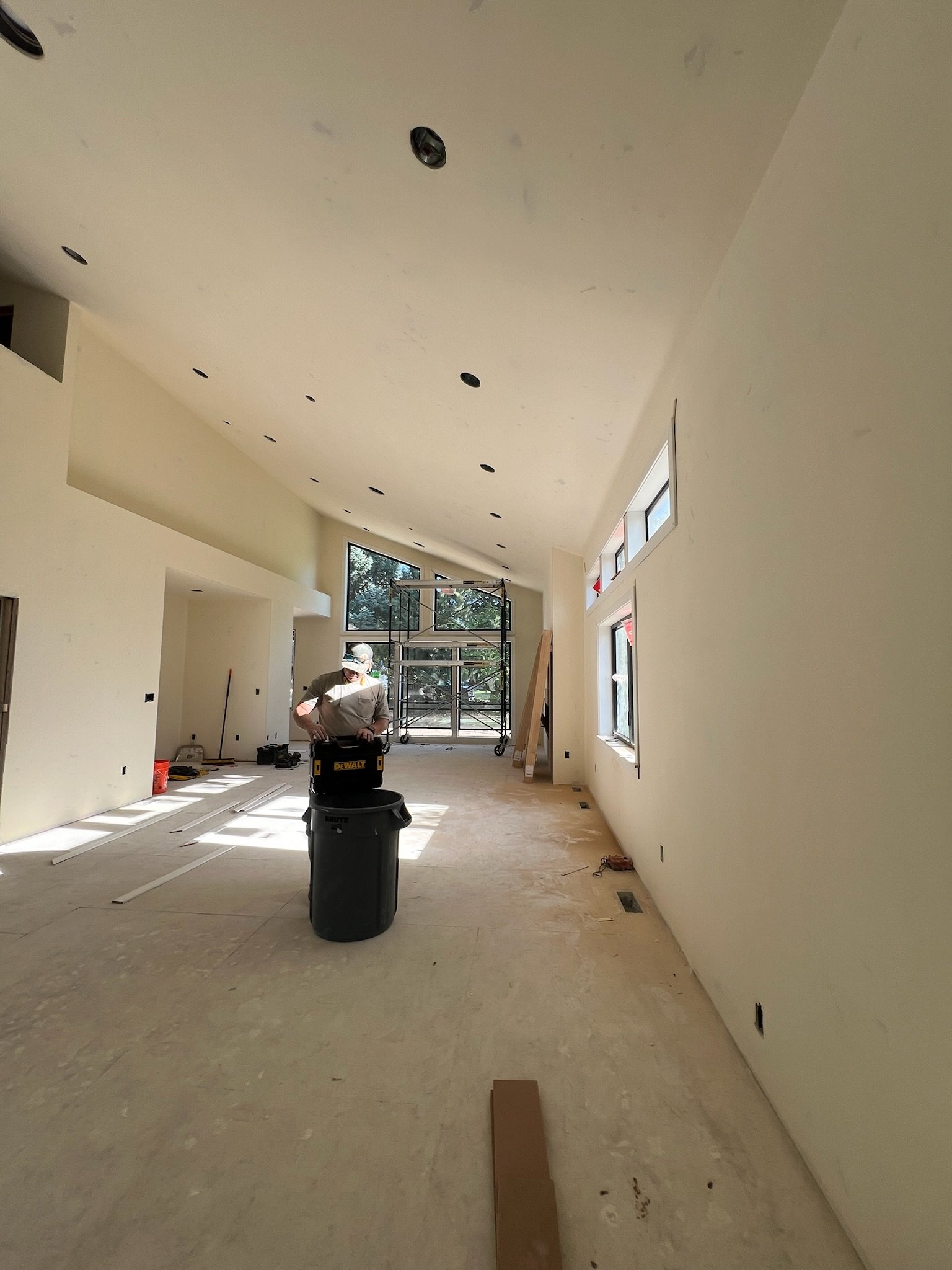 Interior of a room under construction with scaffolding, construction materials, and a large window overlooking a landscape.