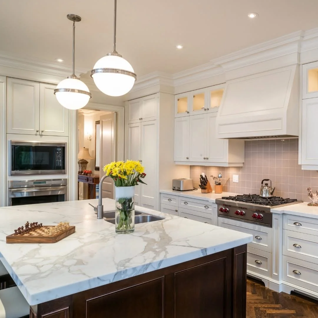 Modern kitchen with white cabinets, marble island countertop, stainless steel appliances, and a vase of yellow flowers.