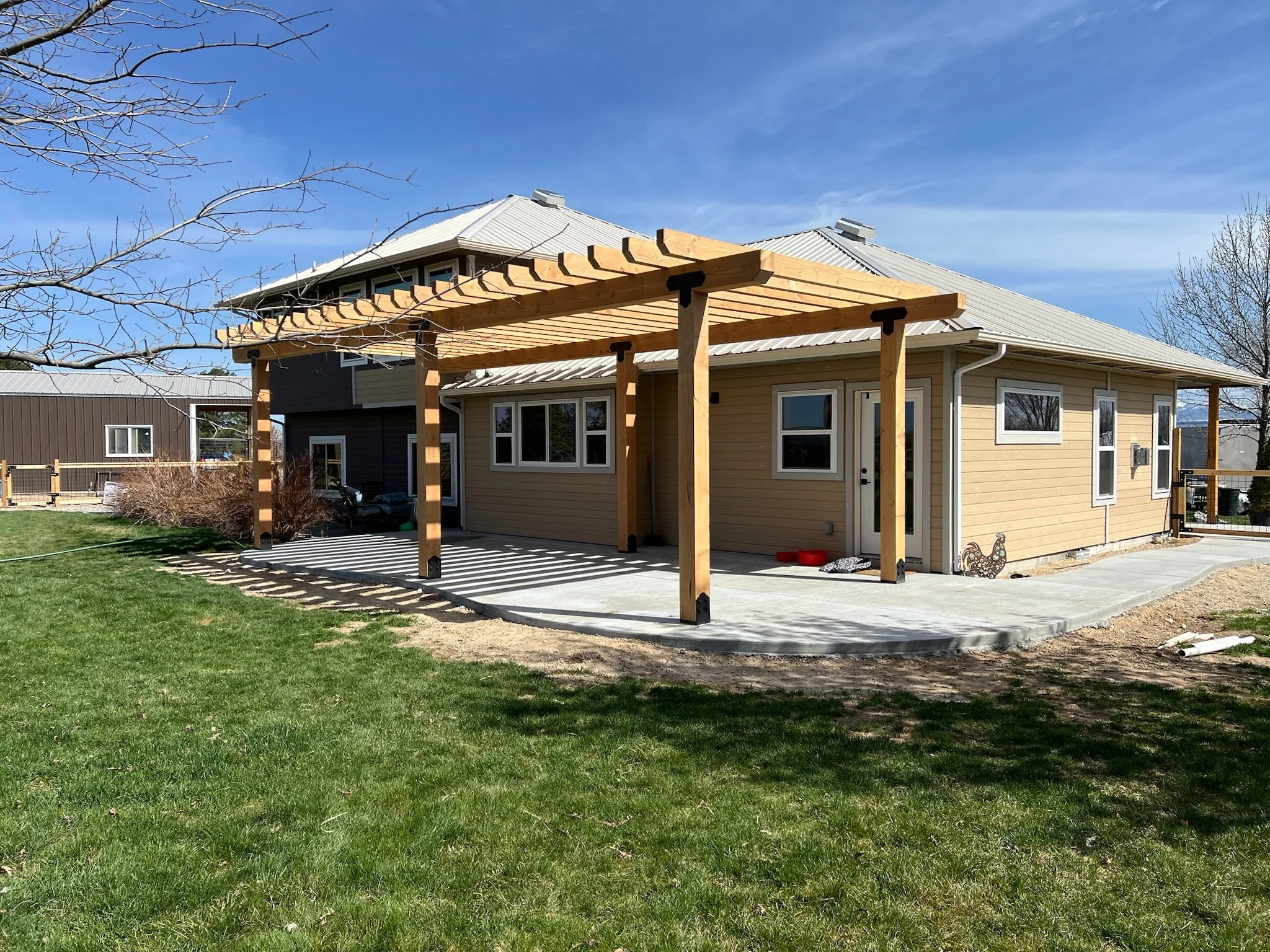 A house with a wooden pergola extending from the back patio under a clear blue sky.