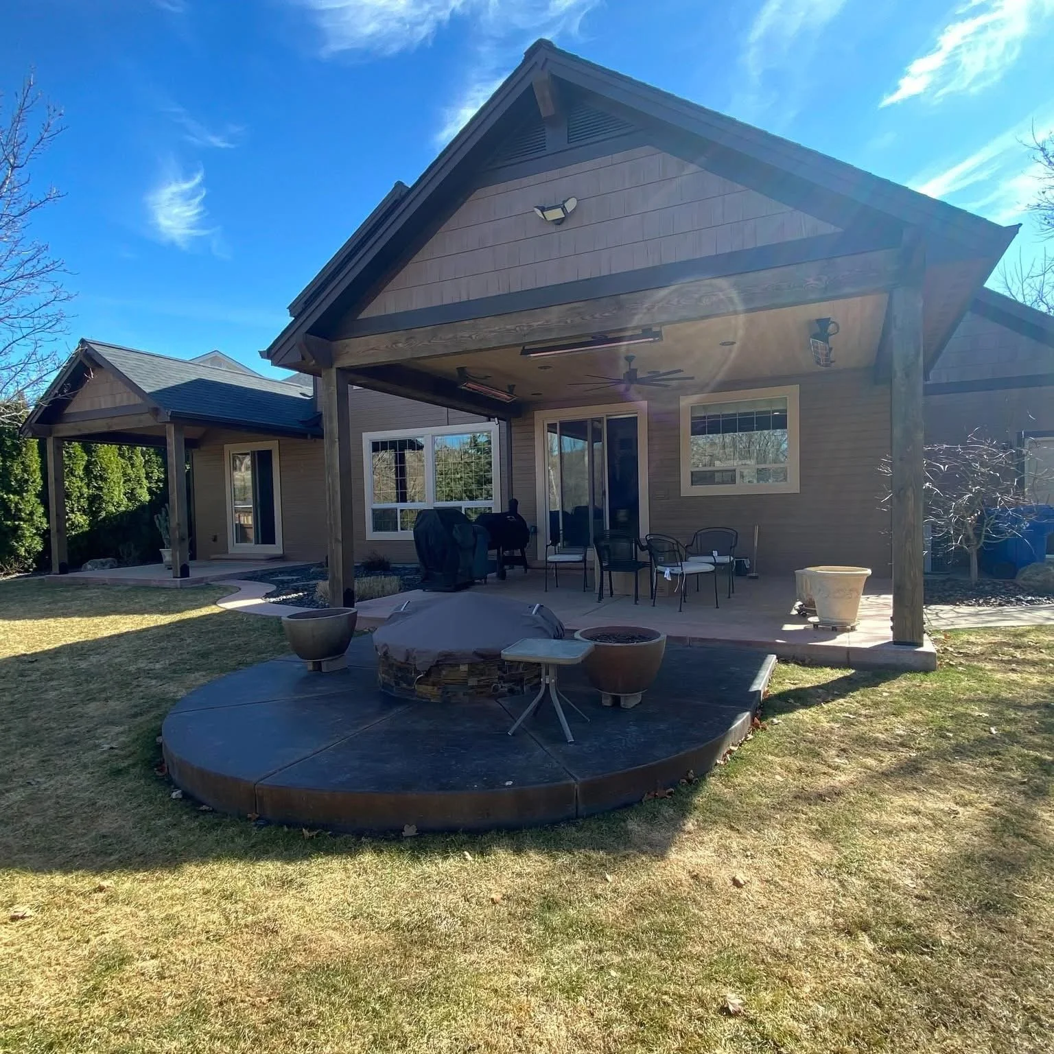 Backyard of a house with a covered patio, outdoor furniture, and a hot tub on a round platform.