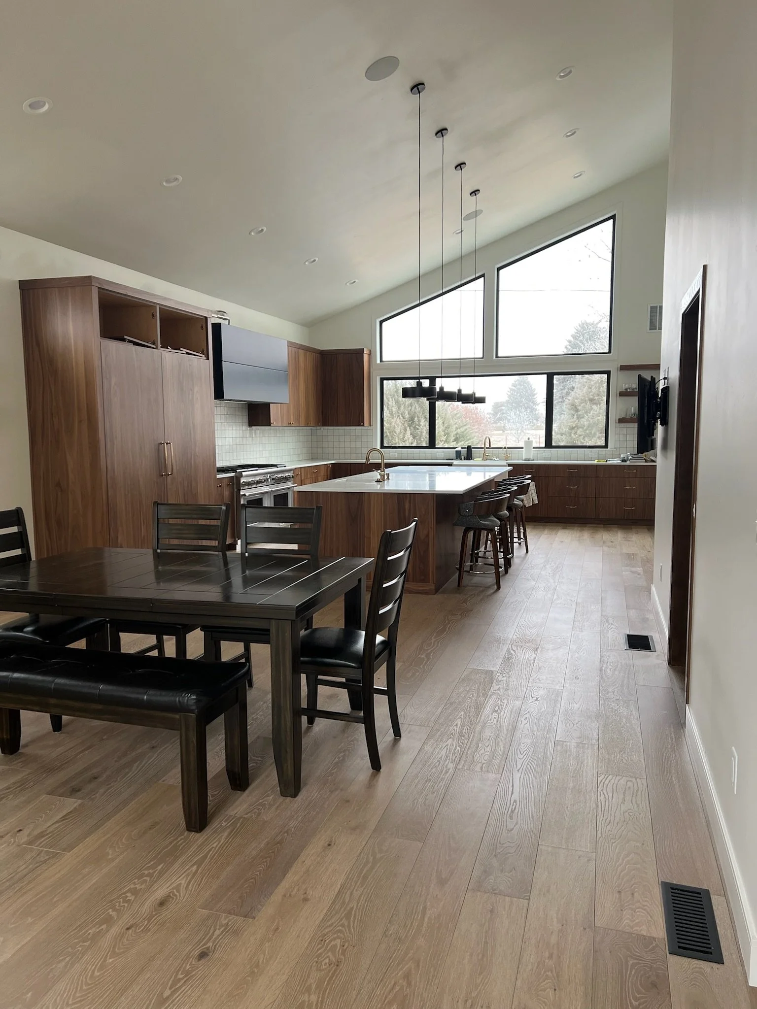 Modern kitchen with wood cabinets, a large white island, and large windows with a view of trees.