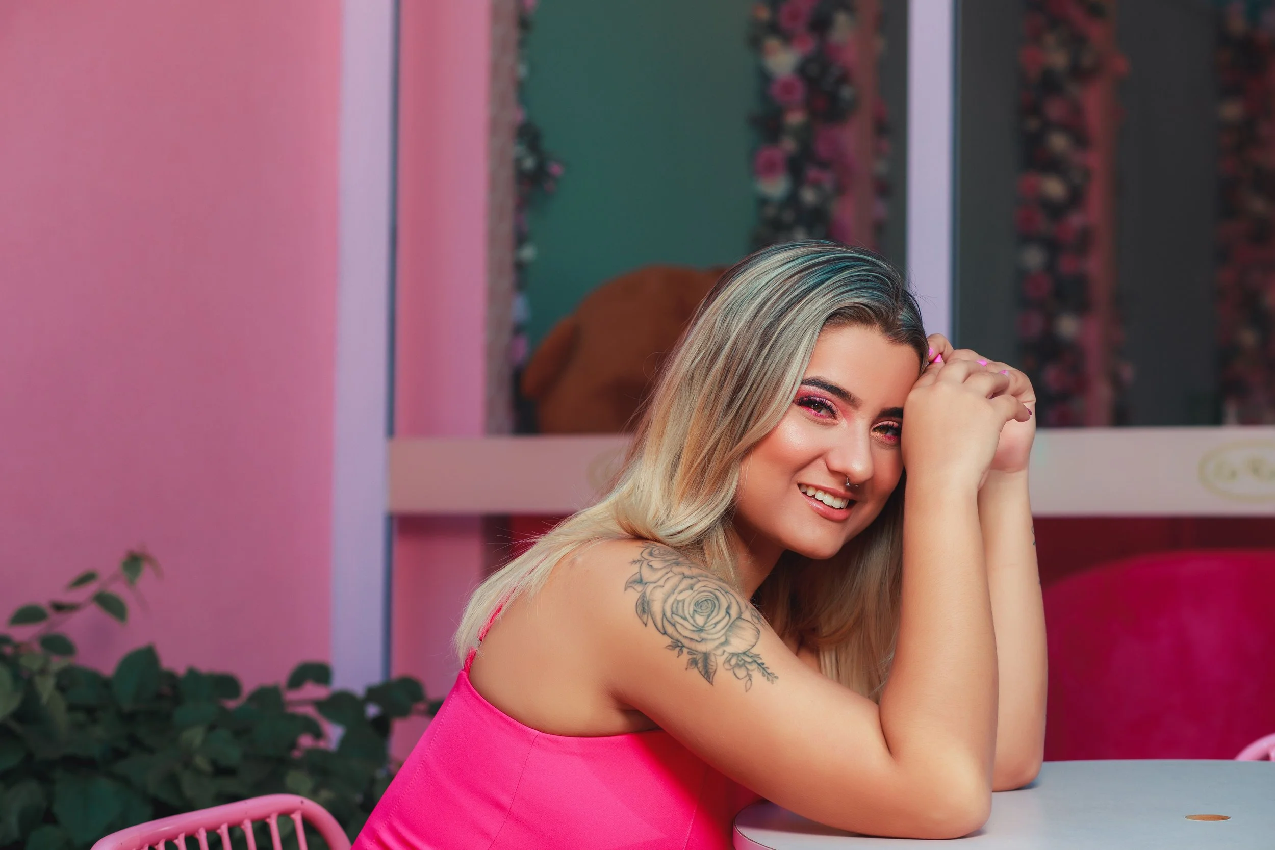 A smiling woman with dark hair in a casual pink shirt sitting and looking directly at the camera, conveying a warm and approachable tone.