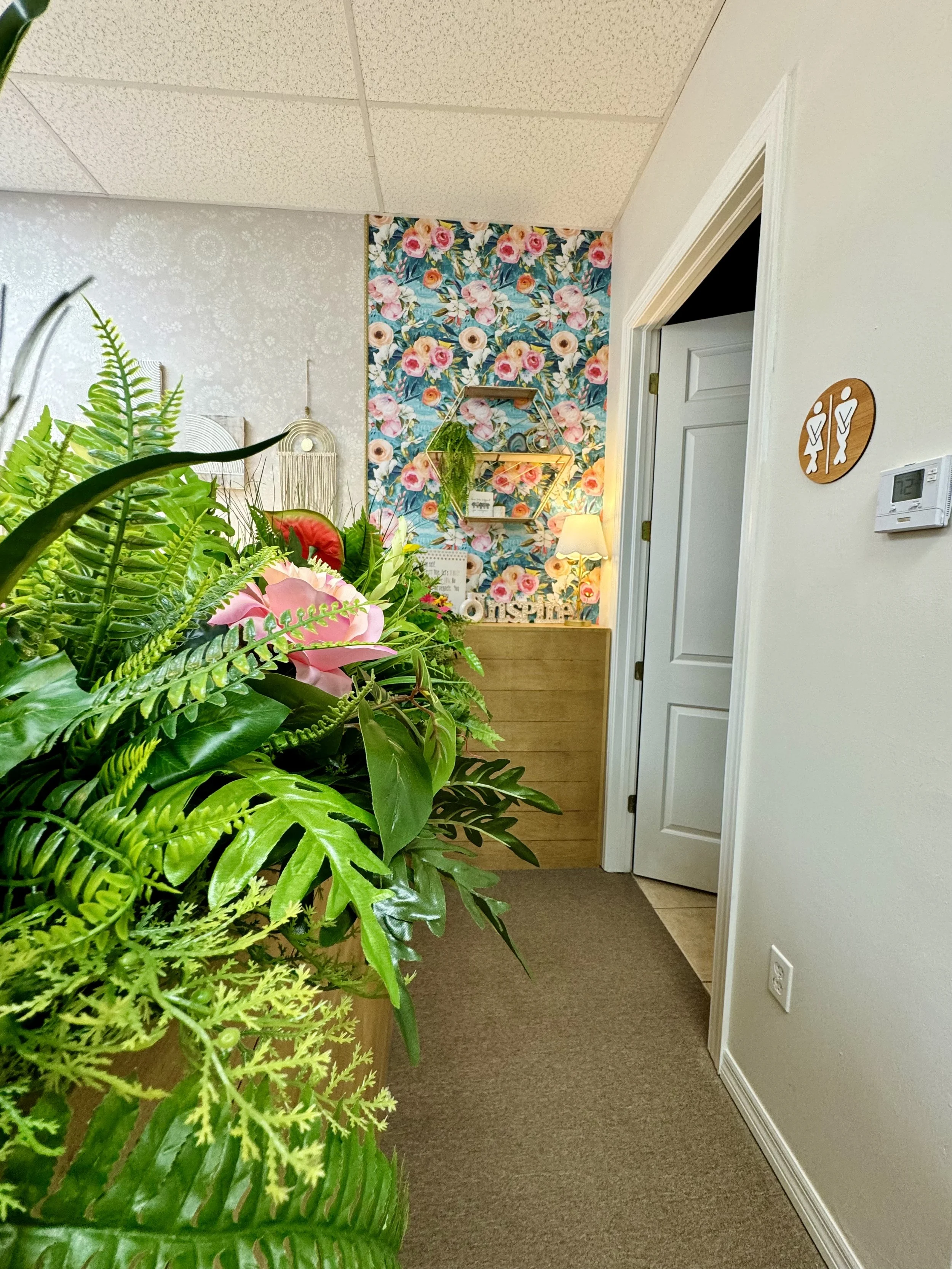 Interior of a therapy room with a floral accent wall, and a wall sign indicating restrooms.