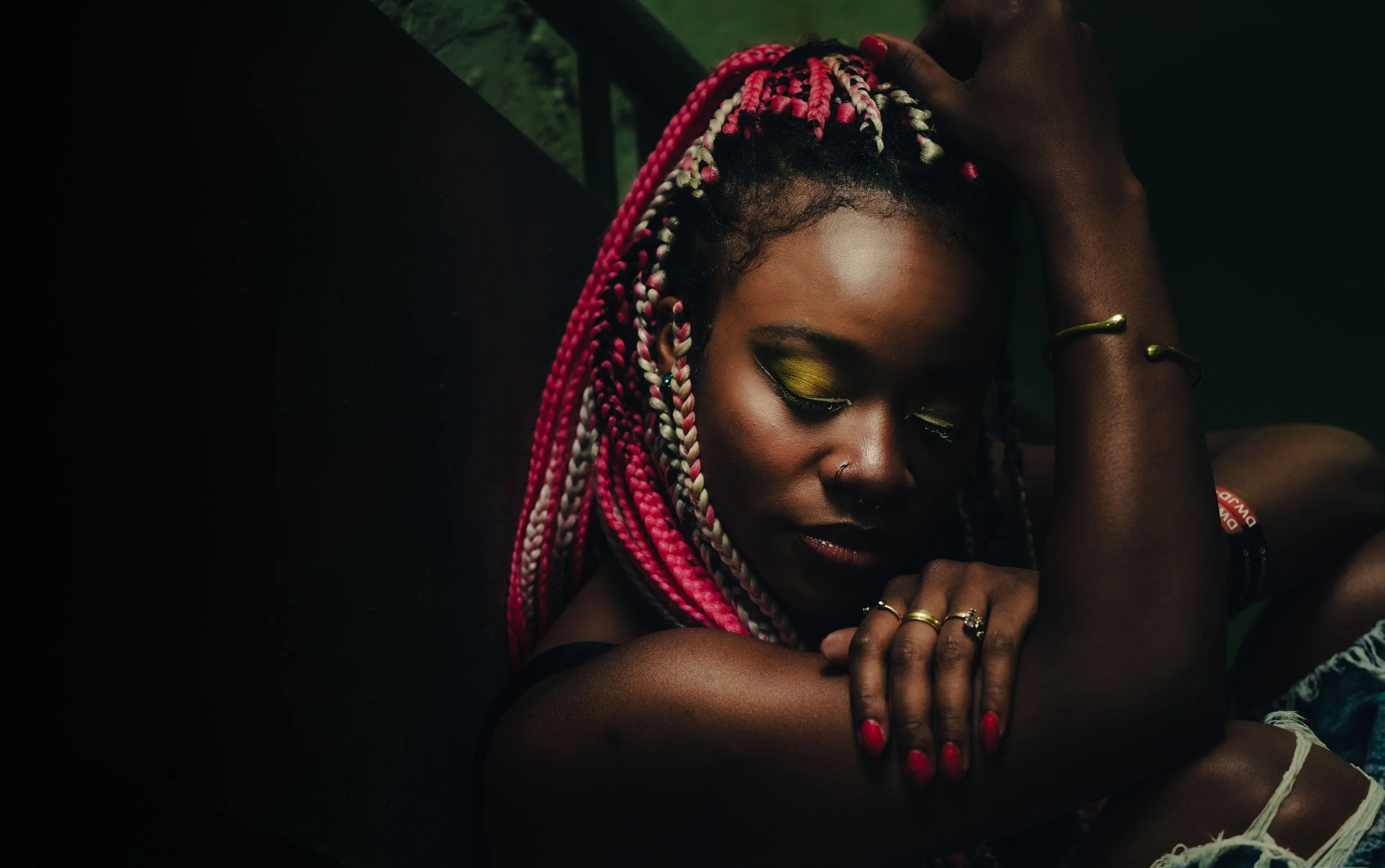 Black woman with pink braids and bold eye makeup sitting in low light, eyes closed, head resting on her arm in a quiet moment of inward reflection -- is EMDR only for trauma and what it actually treats beyond PTSD | EMDR Trauma Therapist Cape Coral