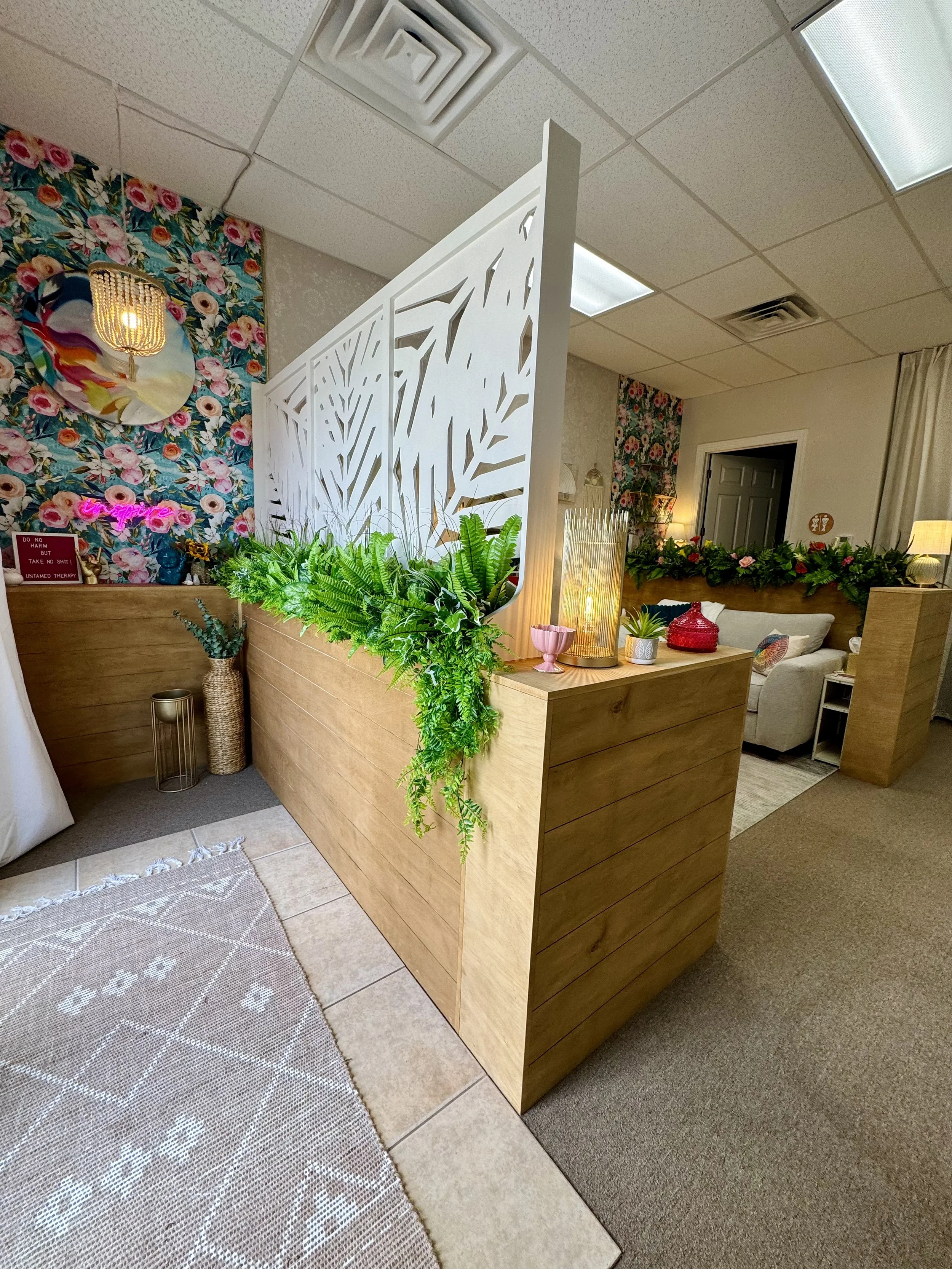 Indoor welcoming space with a wooden partition decorated with green plants, separating trauma therapy office with and various decorative items including lamps and vases.