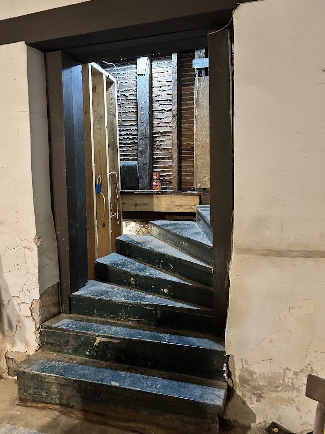 A staircase with black steps leading up to a partially finished room with wooden walls and construction materials.
