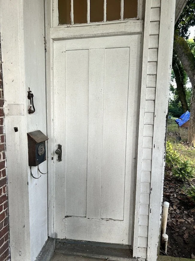 White wooden exterior door with a small window at the top, a vintage wall-mounted telephone to the left, and an old-fashioned door handle and lock.