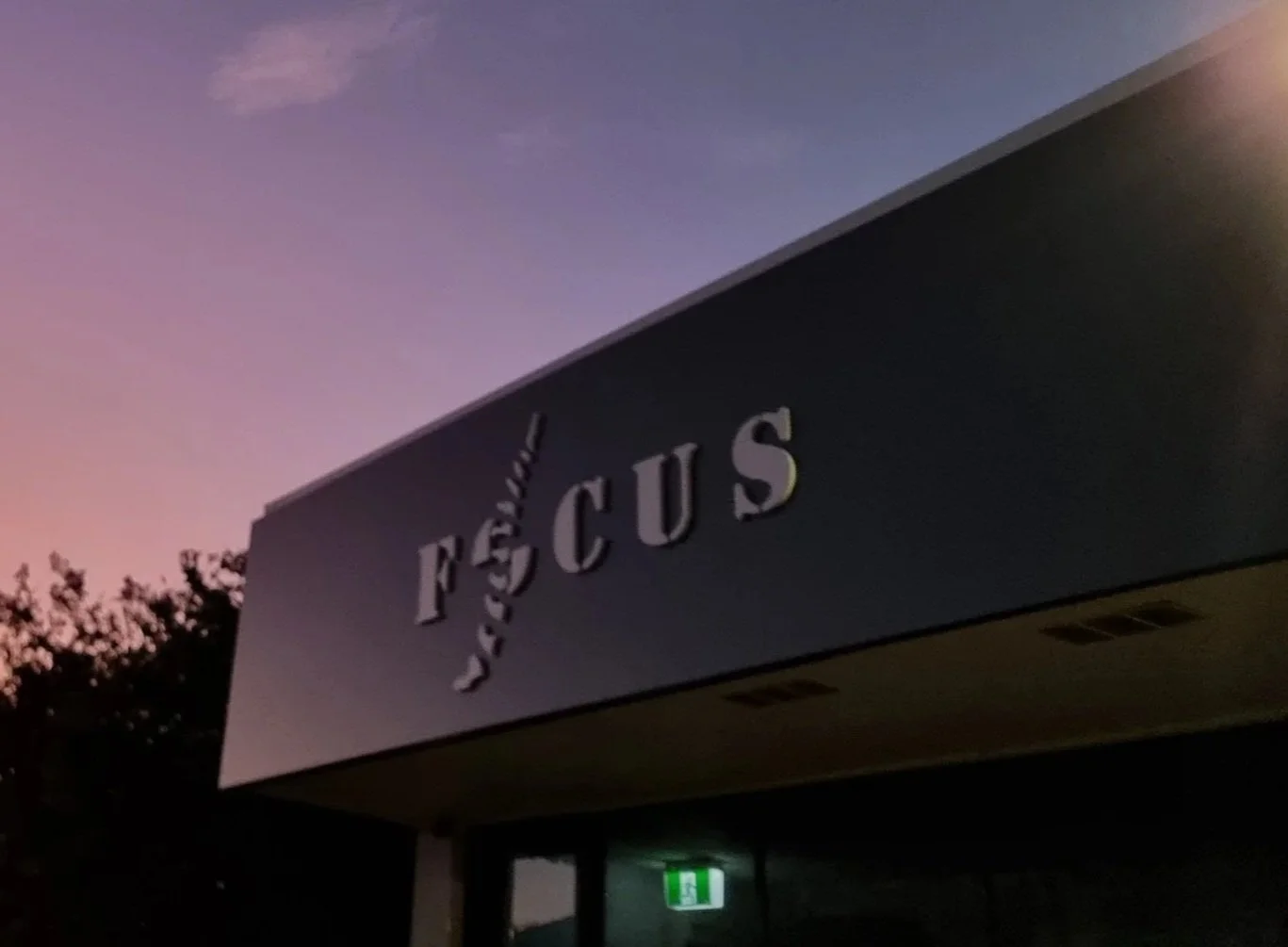 A sign on a dark building with the word 'FUS' and the phrase 'Darkside' above it, against a purple and pink sunset sky.