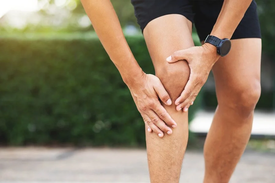 A person in athletic clothing holding their knee, indicating knee pain or injury.