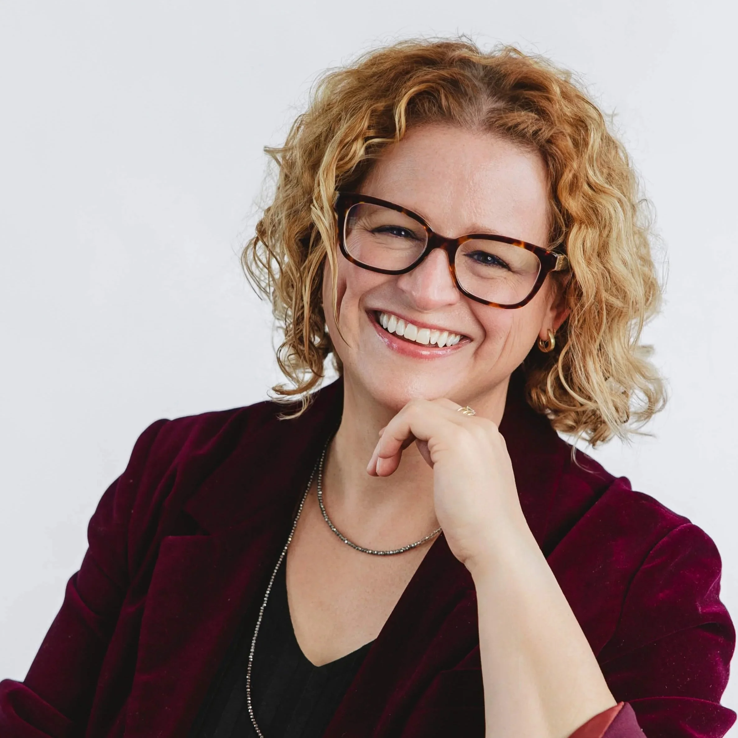Dani Beam of Relay Community Benefit Solutions is smiling with her hand near her chin against a plain white background.