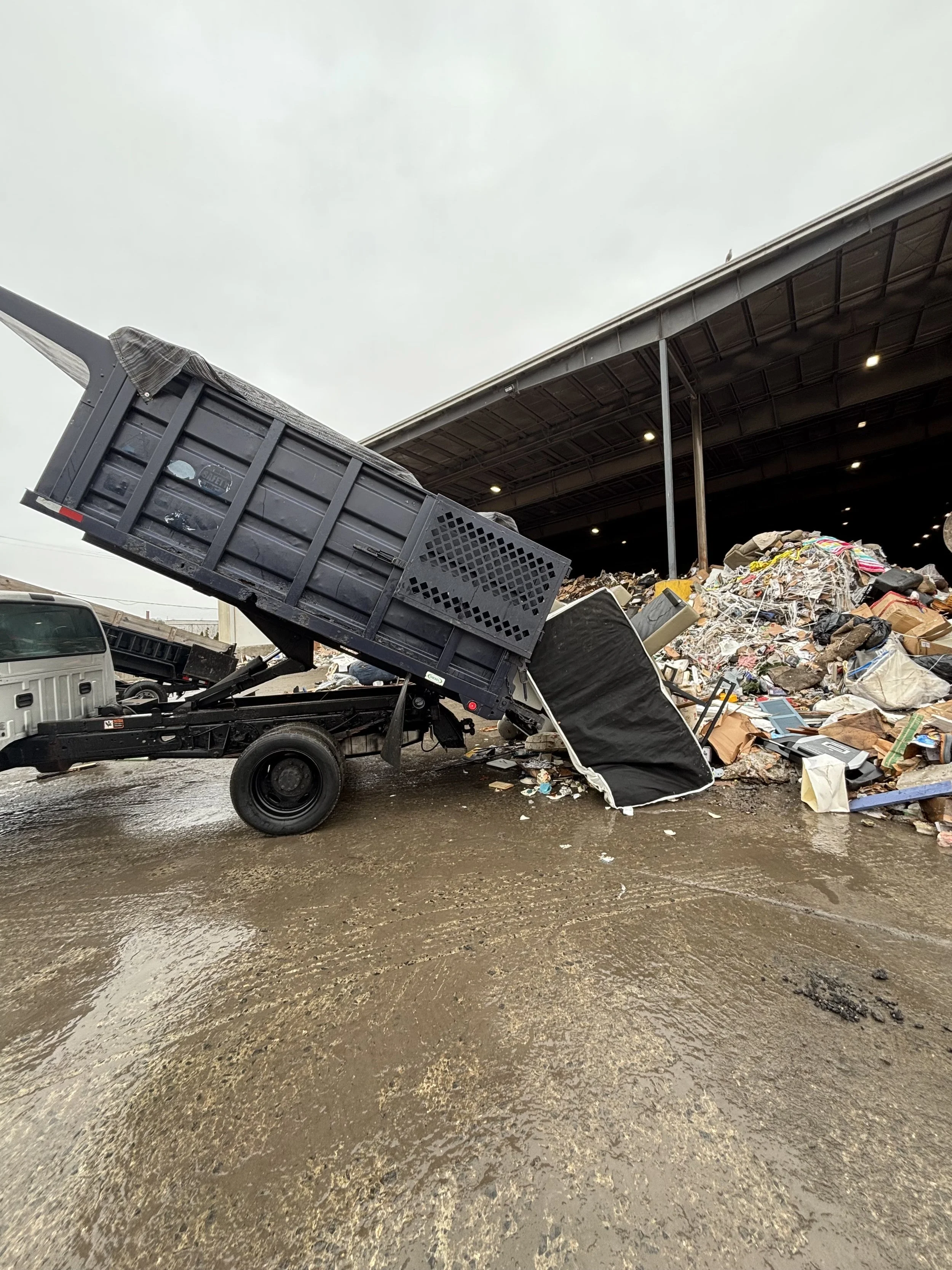 Dump truck unloading trash and recyclables into a large indoor waste pile
