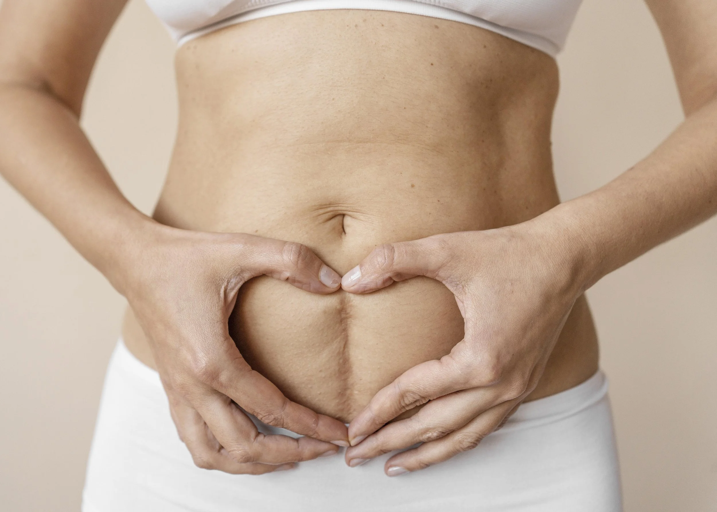 A woman's bare midsection with her hands forming a heart shape over her stomach.