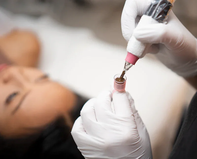 A person receiving a cosmetic injection or treatment in a medical setting, with a focus on the vial and syringe, while the patient is lying down with their eyes closed.