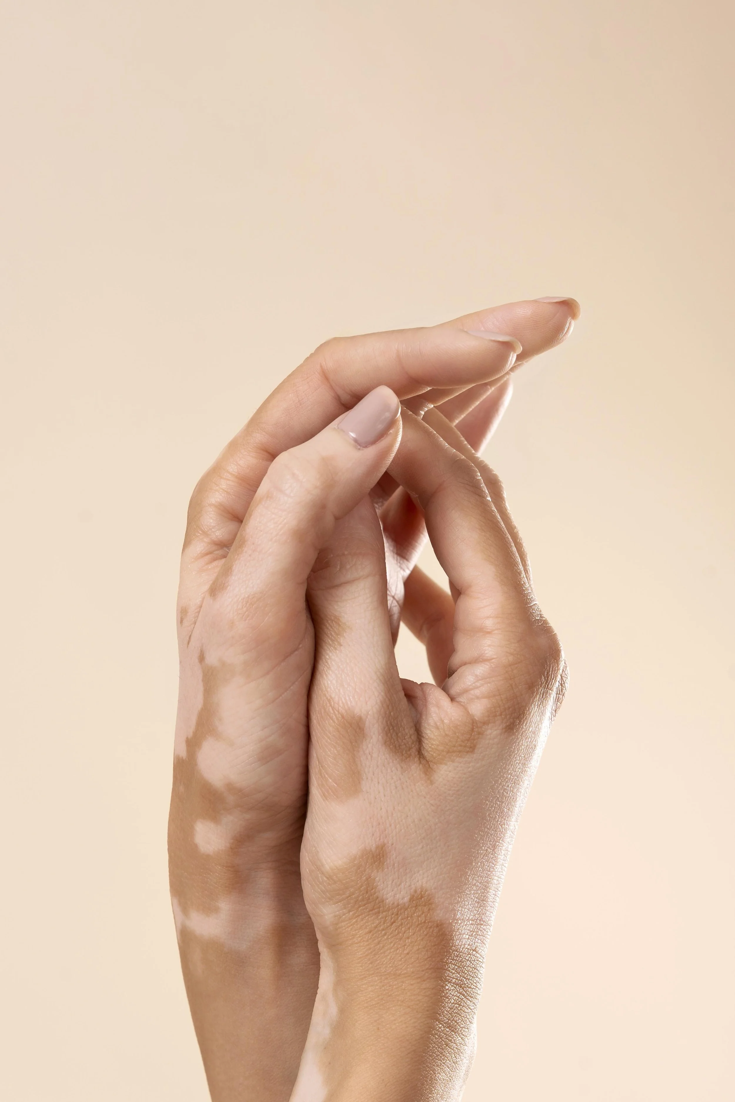 Close-up of two hands with one hand gently holding the other, set against a neutral background.