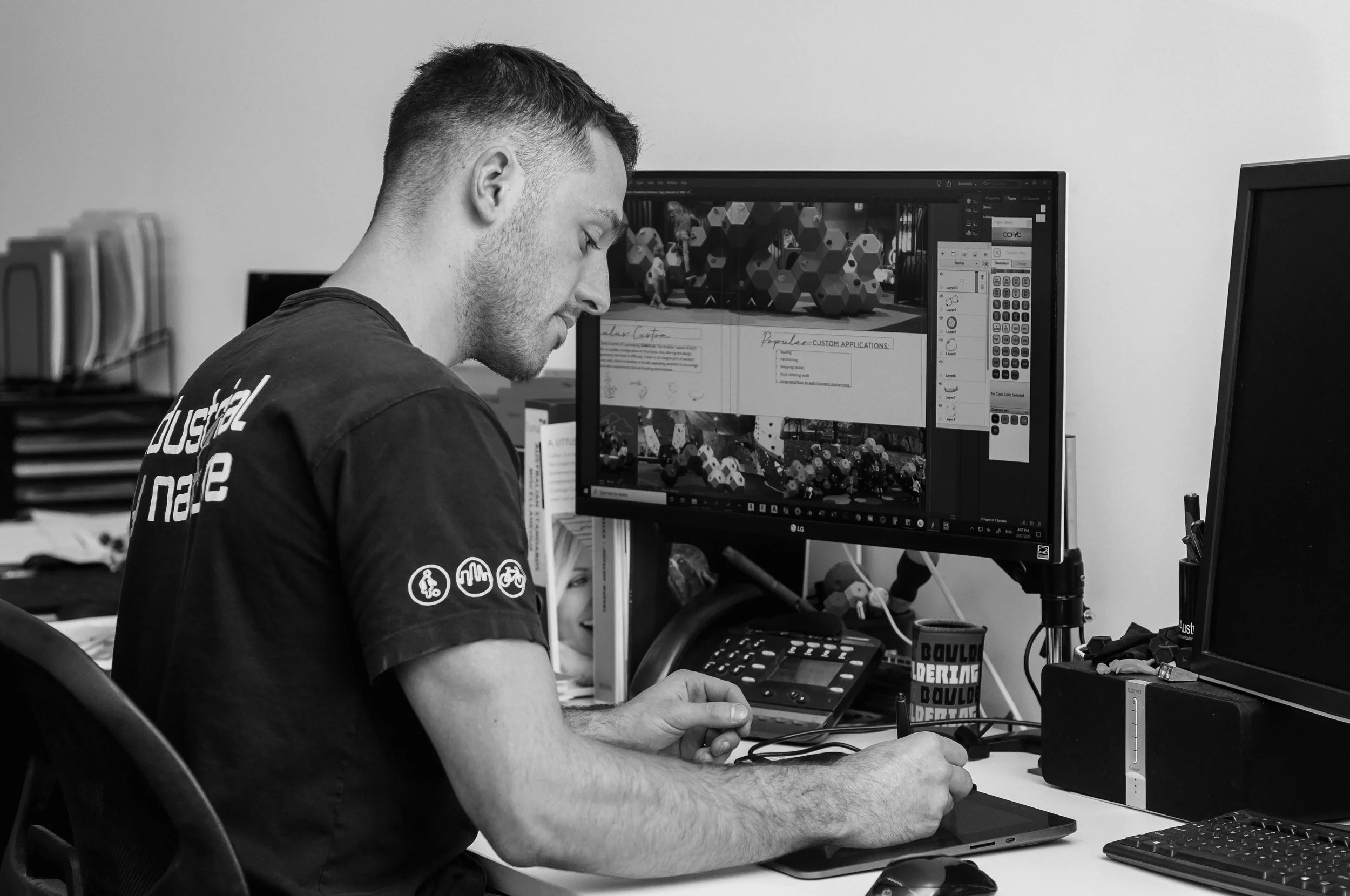 A young man with short hair working at a desk with dual computer screens, designing bouldering structures