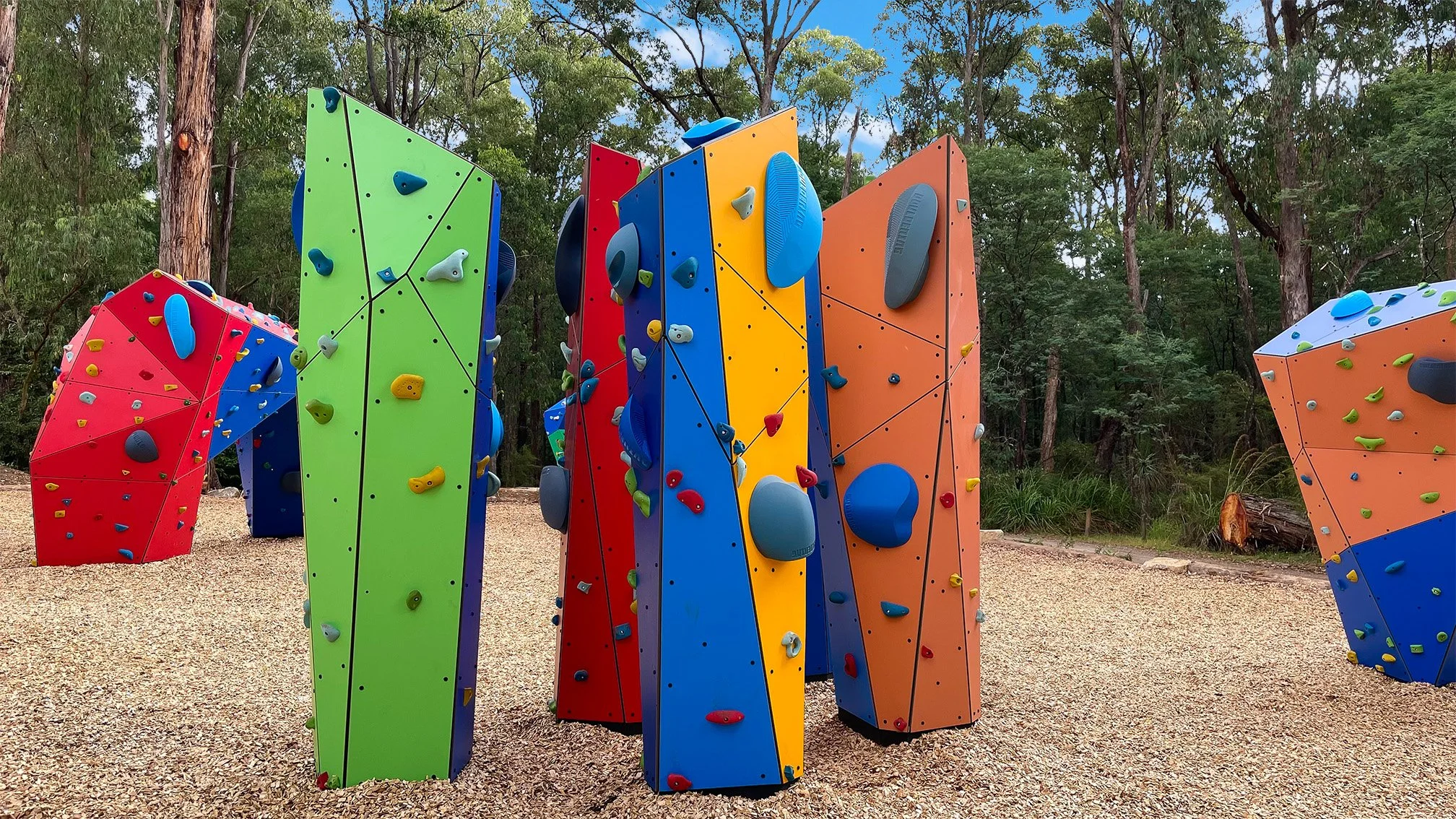 Colorful outdoor bouldering climbing structures in a wooded park.