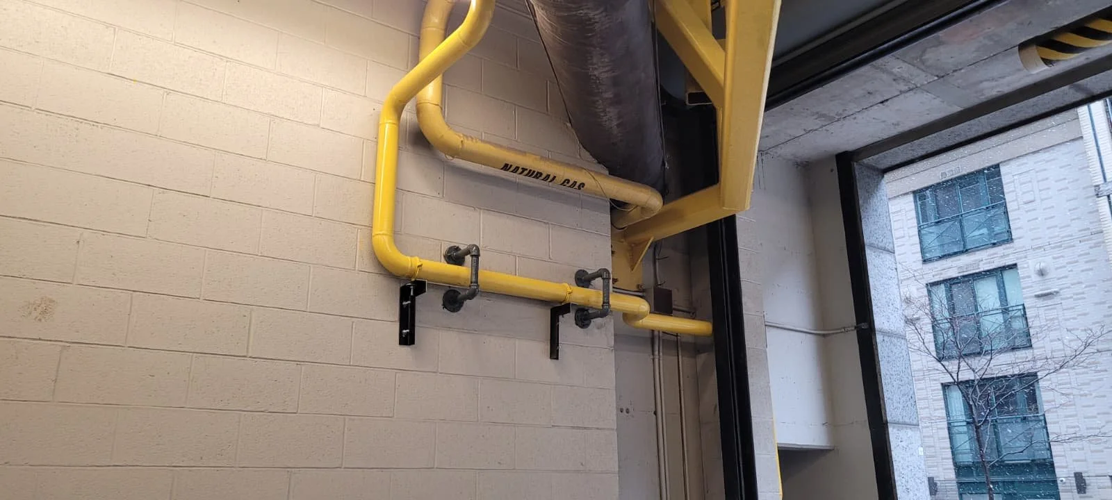 Yellow pipes mounted on a white brick wall next to a window