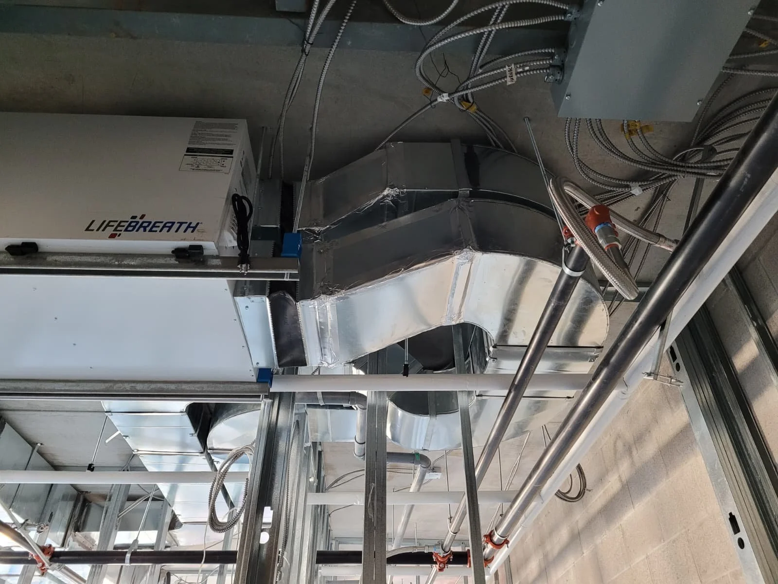 View of industrial HVAC ductwork and electrical wiring in a building's ceiling space.