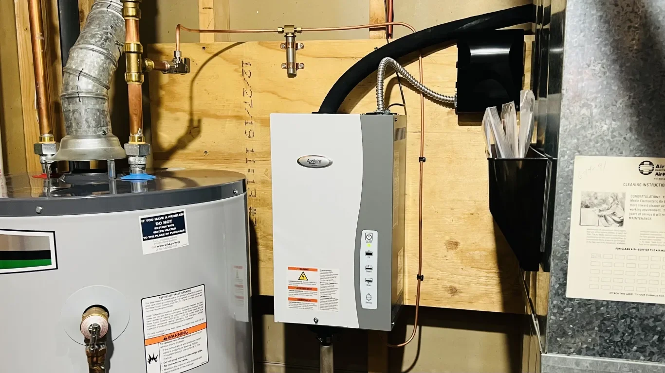 A water heater and a control panel mounted on a wooden wall in a utility room.