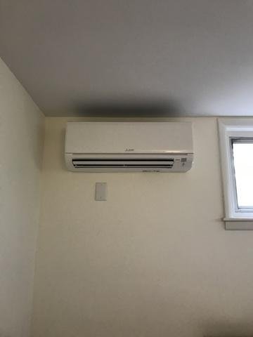 Wall-mounted white air conditioning unit next to a small window in a room with beige walls and ceiling.