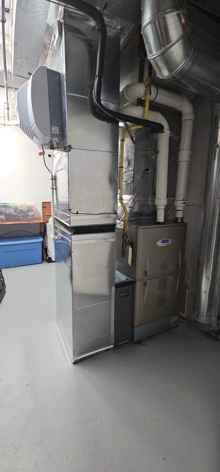 A large industrial HVAC furnace and ductwork system with pipes and vents in a mechanical room.