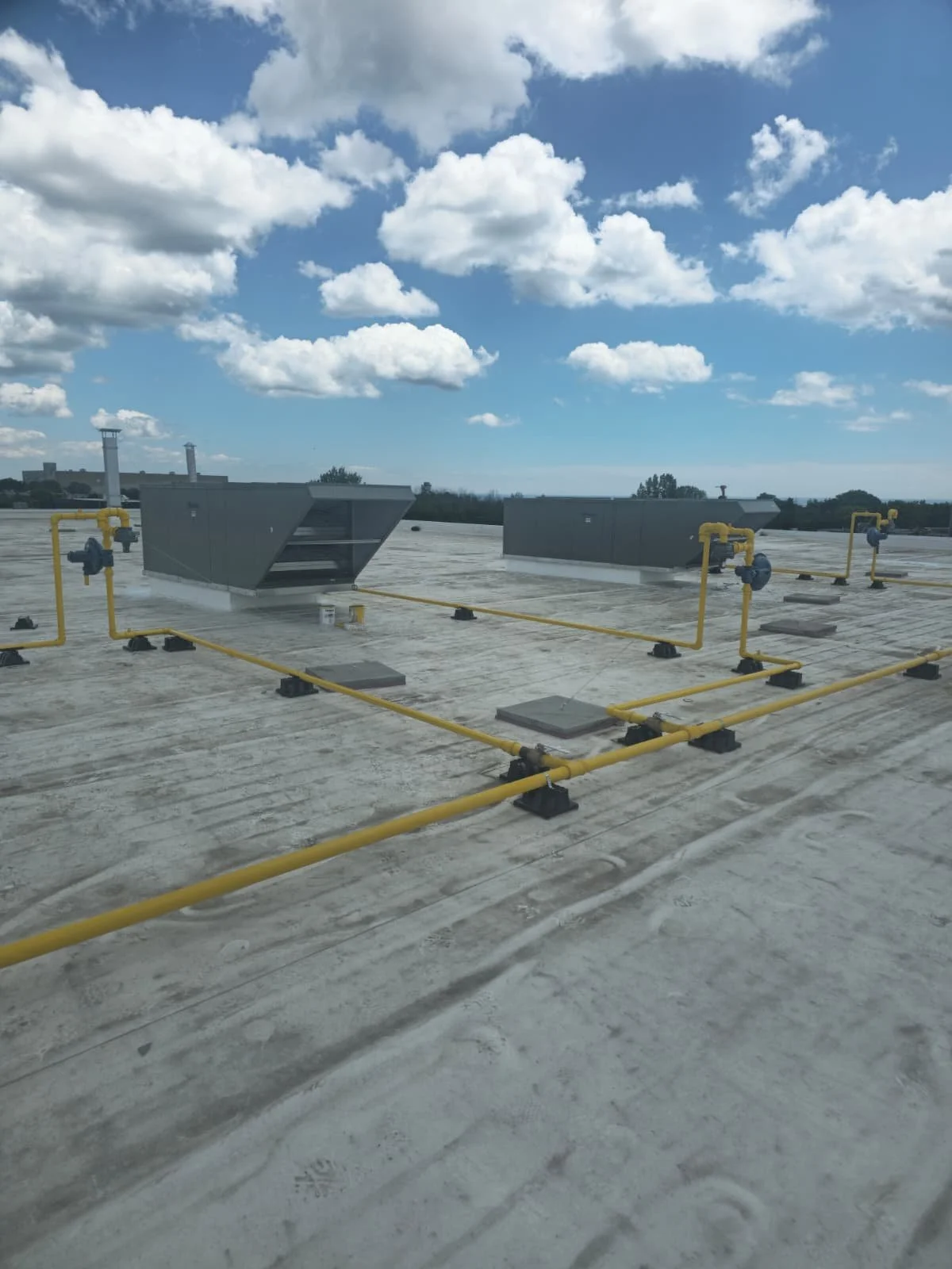 Rooftop with yellow gas pipes, vents, and a cloudy blue sky