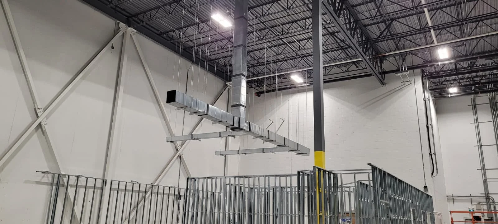 Interior of a large industrial or warehouse building with high ceilings, exposed metal beams, and a ceiling-mounted HVAC system.