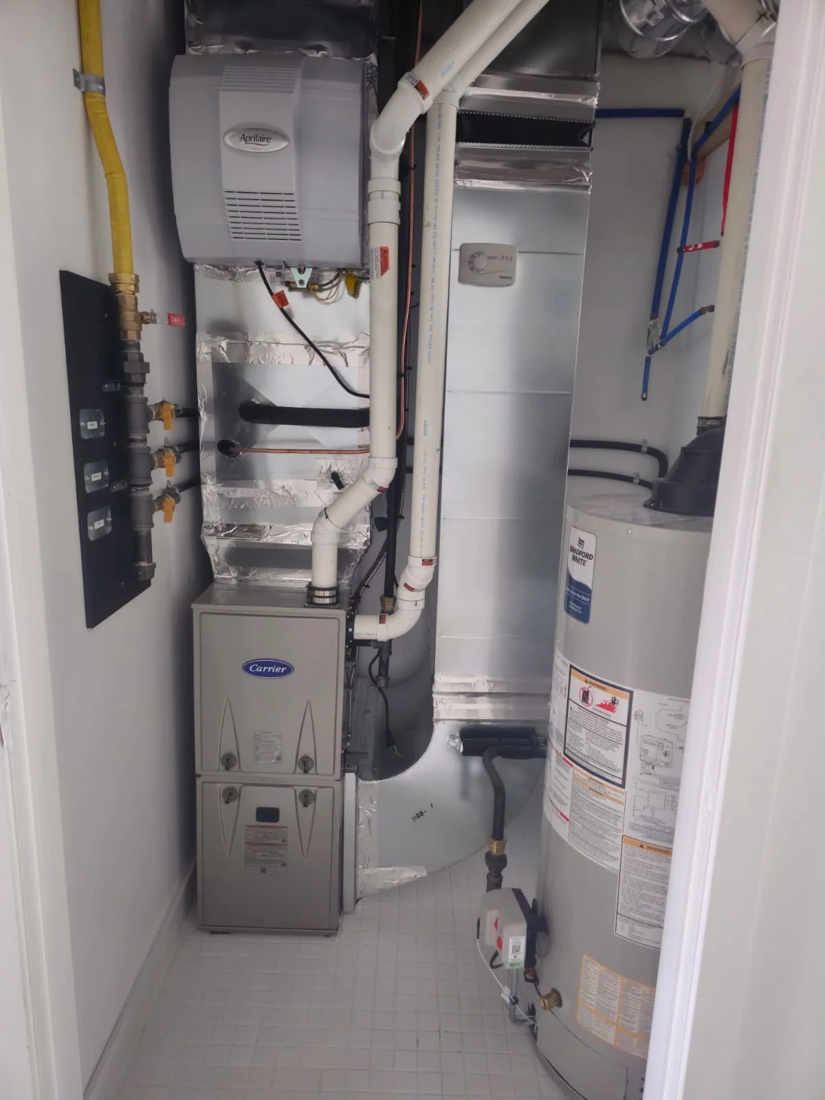 View of a utility closet containing an air handler, water heater, plumbing pipes, and electrical components.
