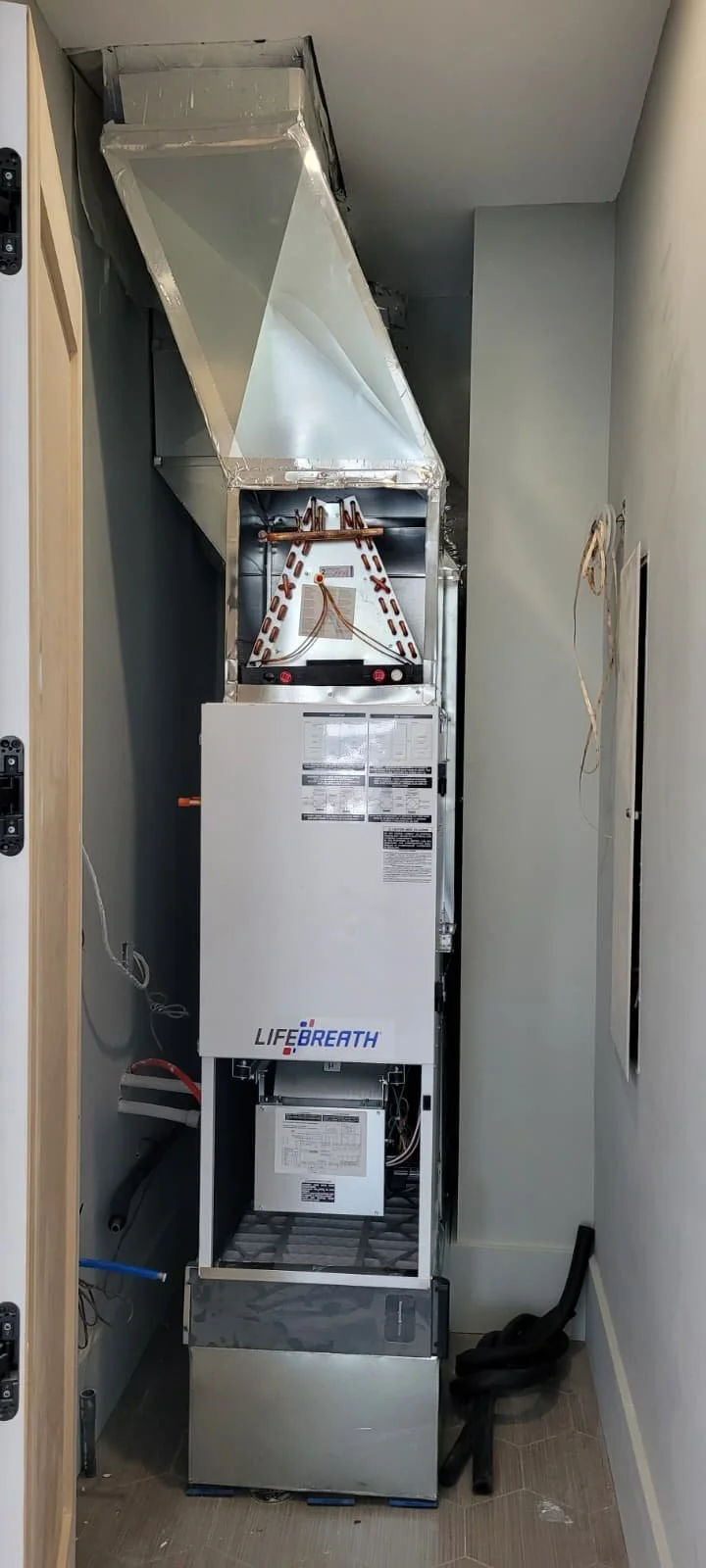 Photo of an furnace system in a closet with ductwork above it.