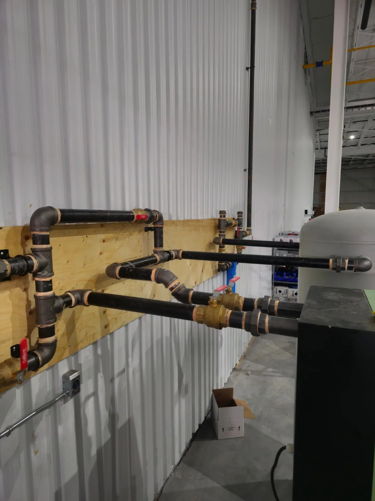 Interior of an industrial facility with plumbing pipes and valves attached to a wooden wall panel.