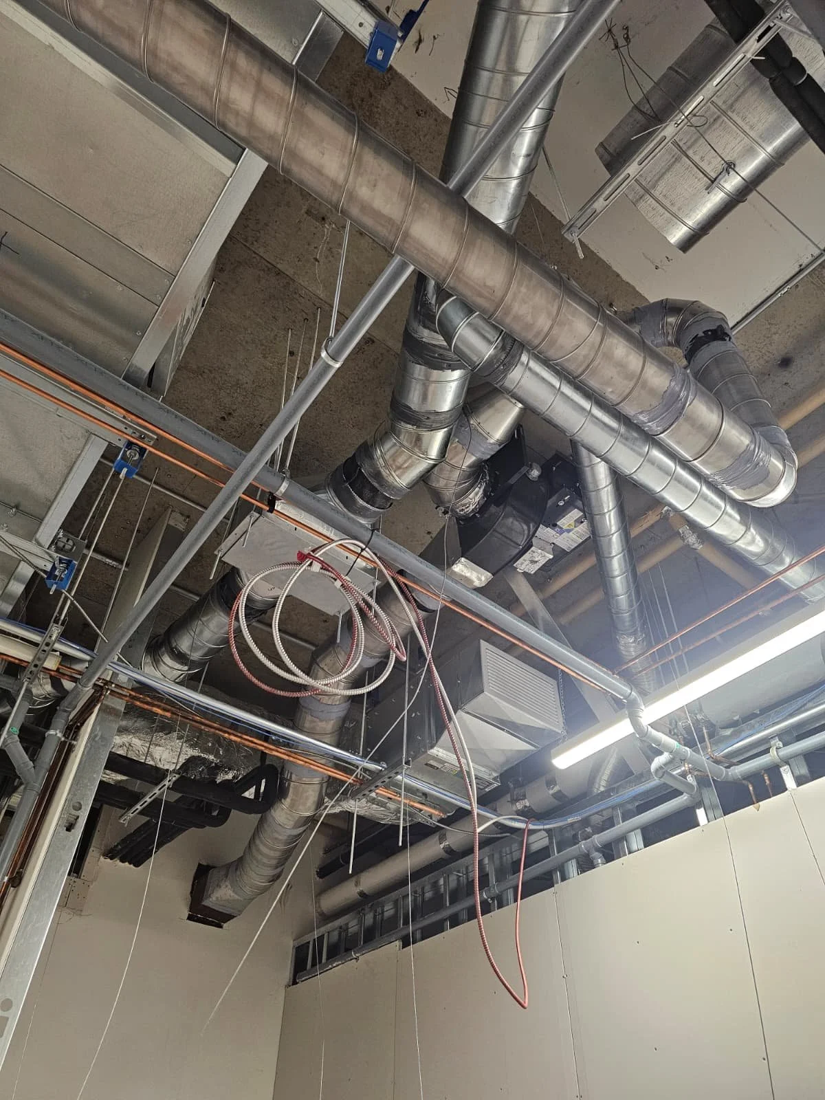 Ceiling with various metal ductwork, pipes, and electrical cables in an industrial or commercial building under construction.